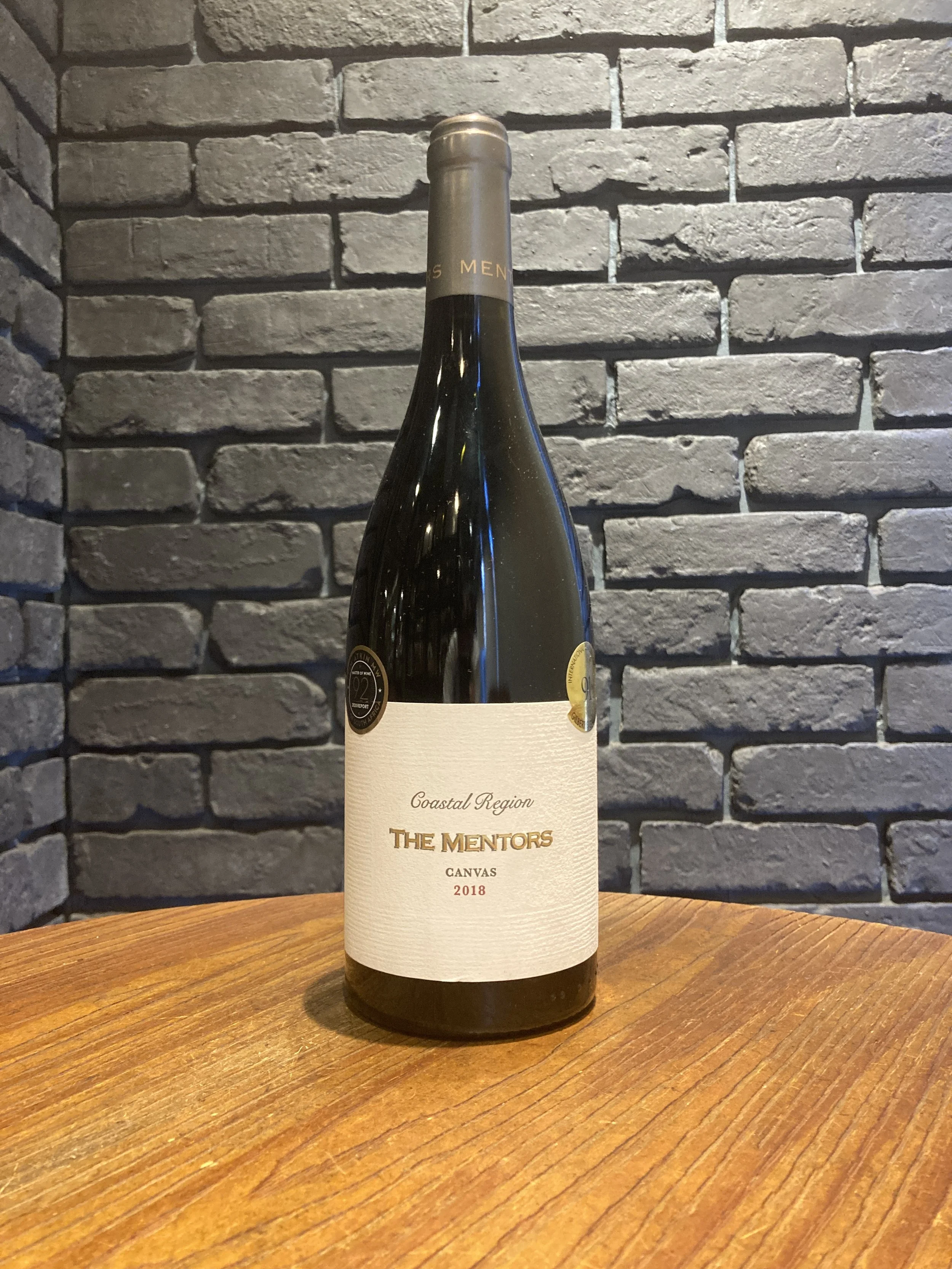 灰色のレンガ壁の前に置かれたワインのボトル、木のテーブルの上に置かれている。