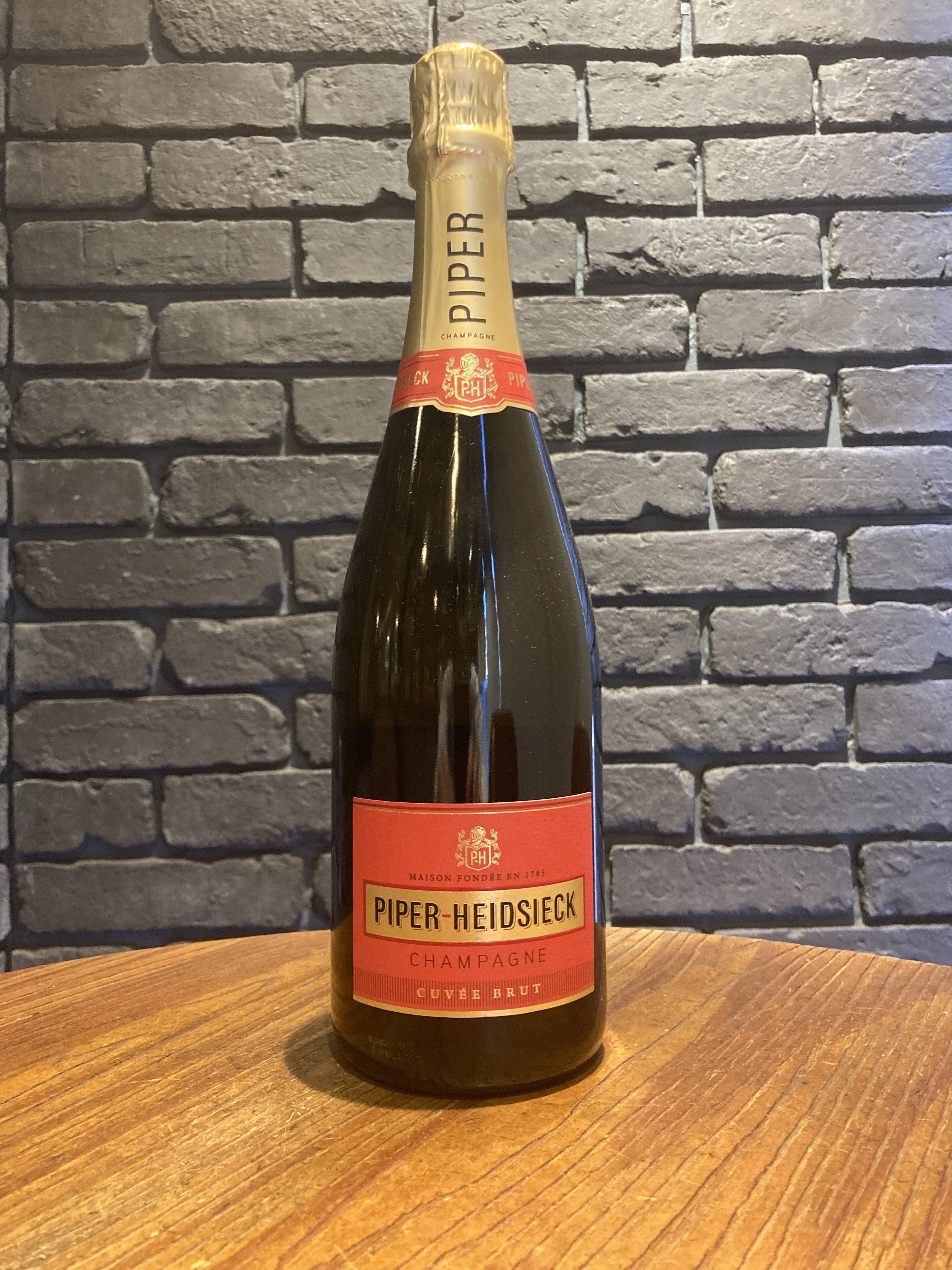 赤いラベルのシャンパンボトルが木製のテーブルの上に置かれている。背景は灰色のレンガ壁である。