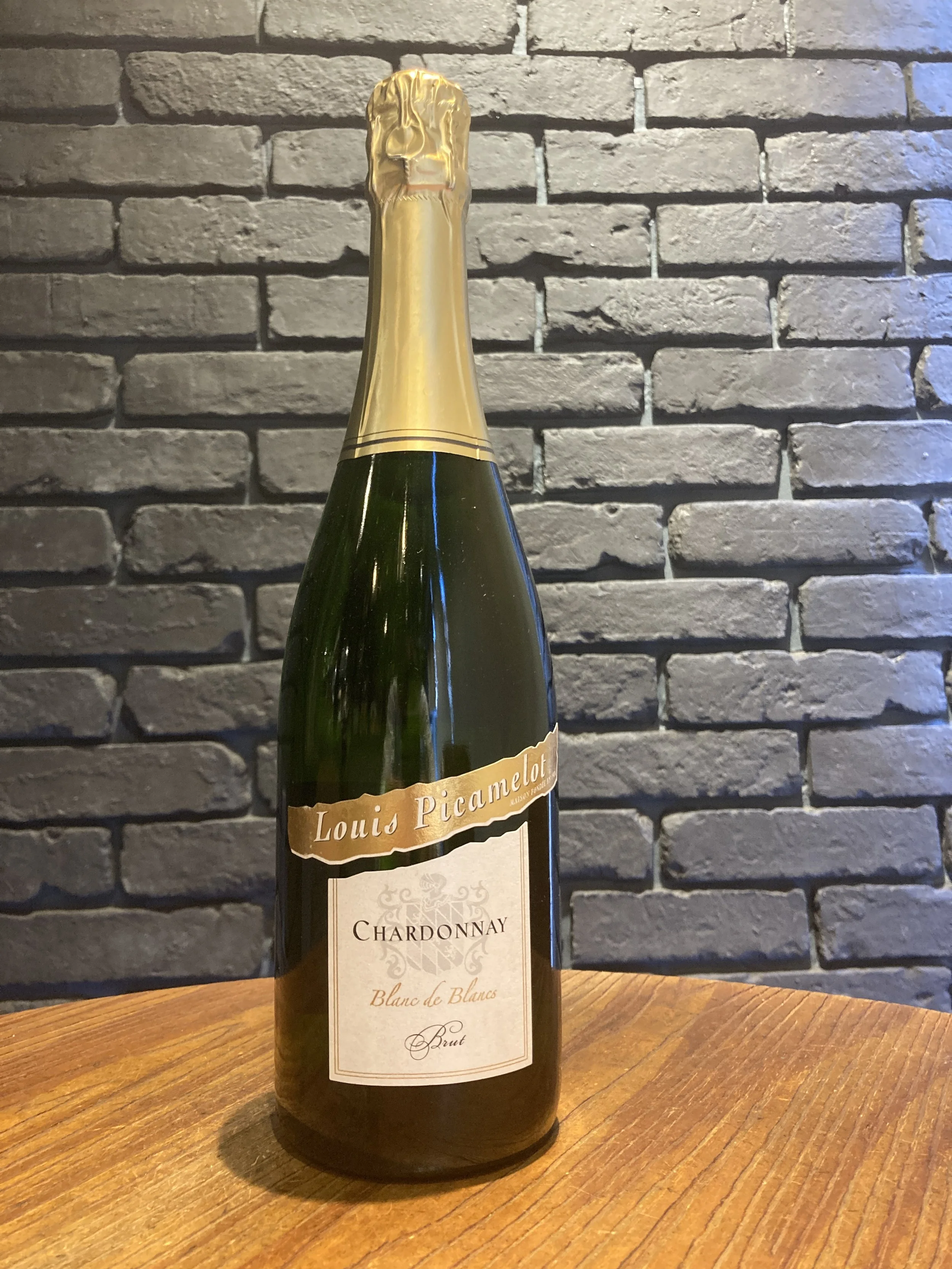 白いラベルのスパークリングワインのボトル、背景は灰色のレンガの壁、ボトルは木製のテーブルに置かれている。