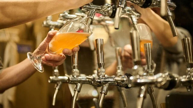ビールサーバーからビールを注いでいる様子で、手に持ったグラスにオレンジ色の飲み物を注いでいるところ