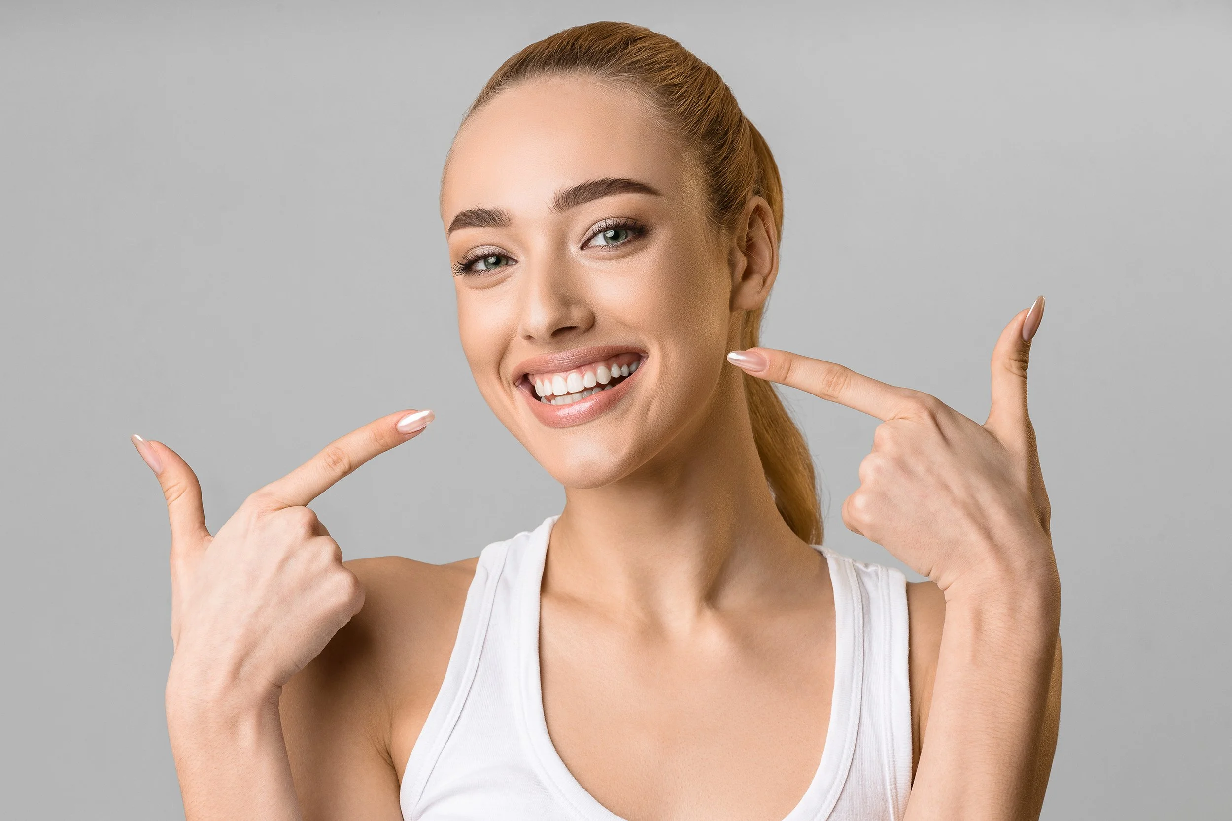 Smiling woman pointing at her perfect teeth, promoting dental health.
