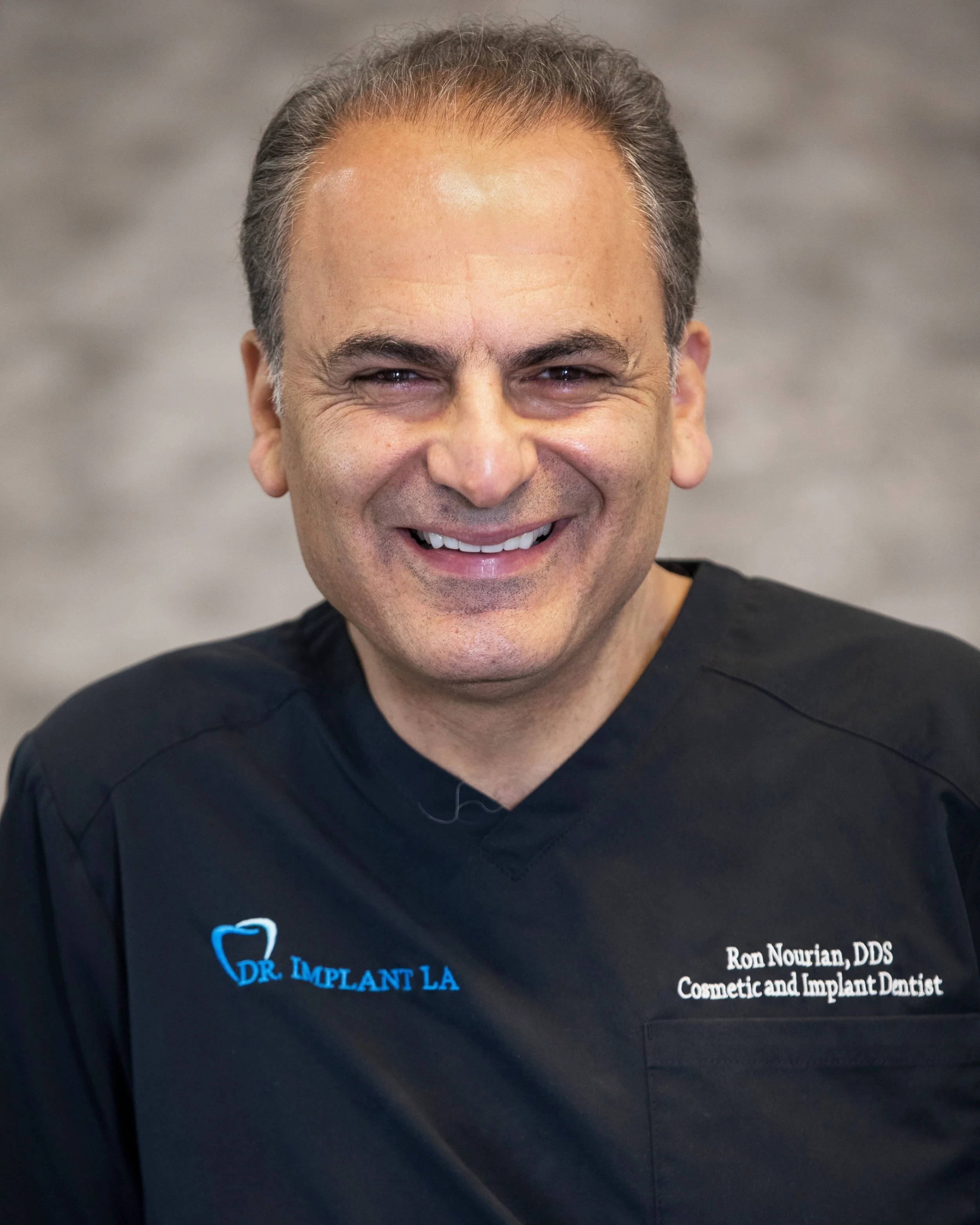 Smiling person in dental scrubs with 'Dr. Implant LA' logo.