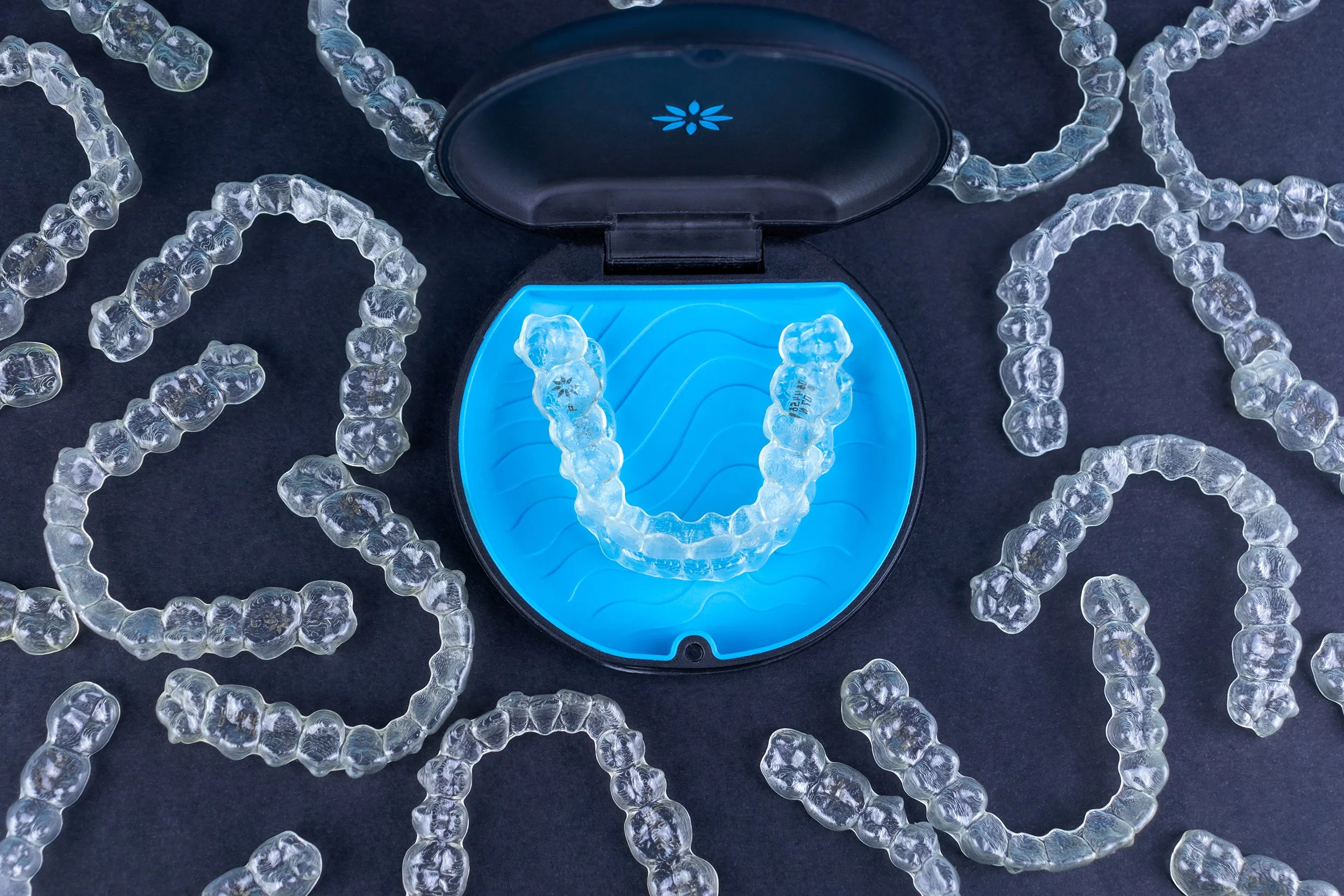 Clear aligners and a blue case on a dark surface, showcasing orthodontic dental trays used for straightening teeth.