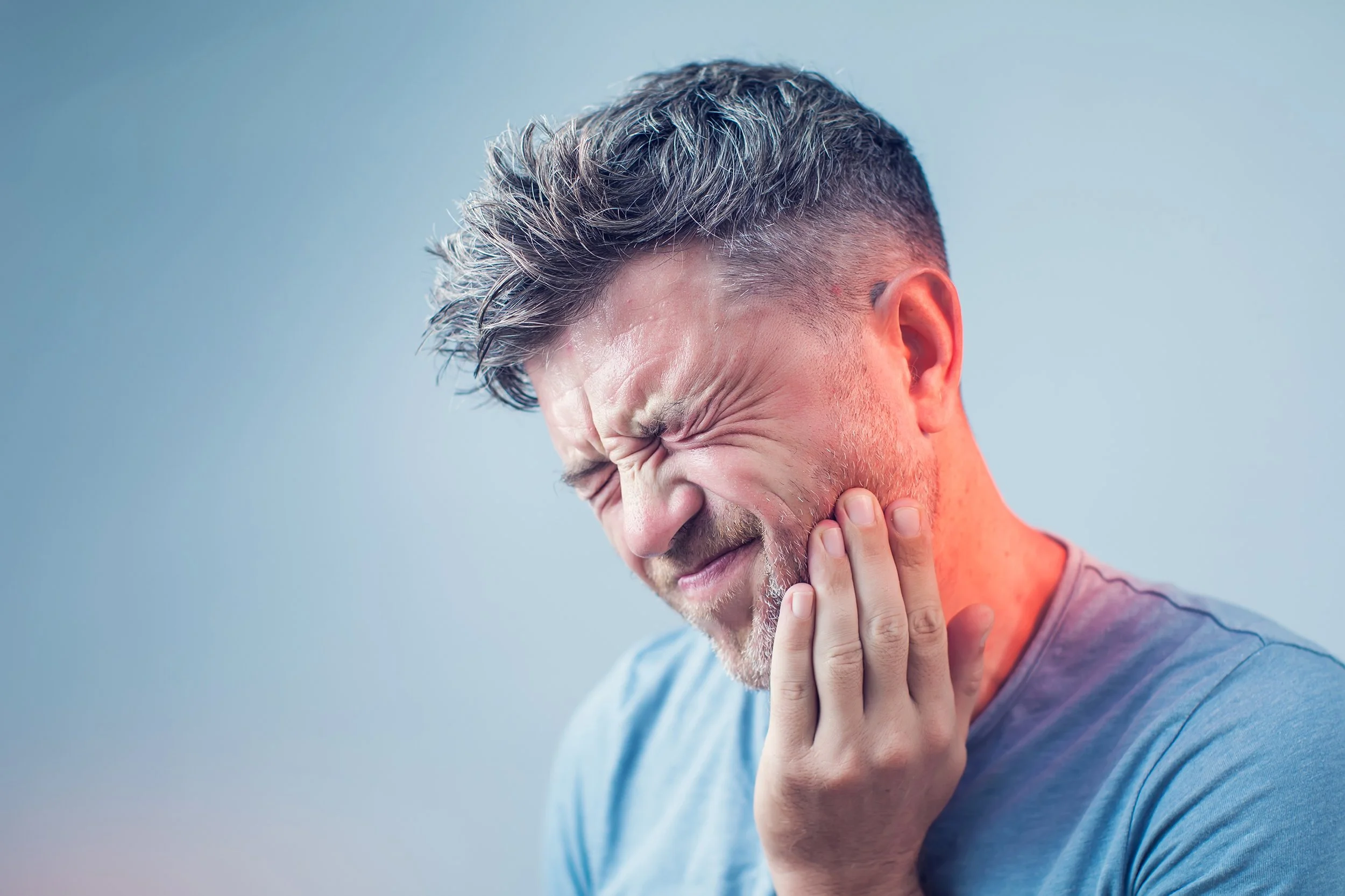 Man with toothache holding his jaw, grimacing in pain.