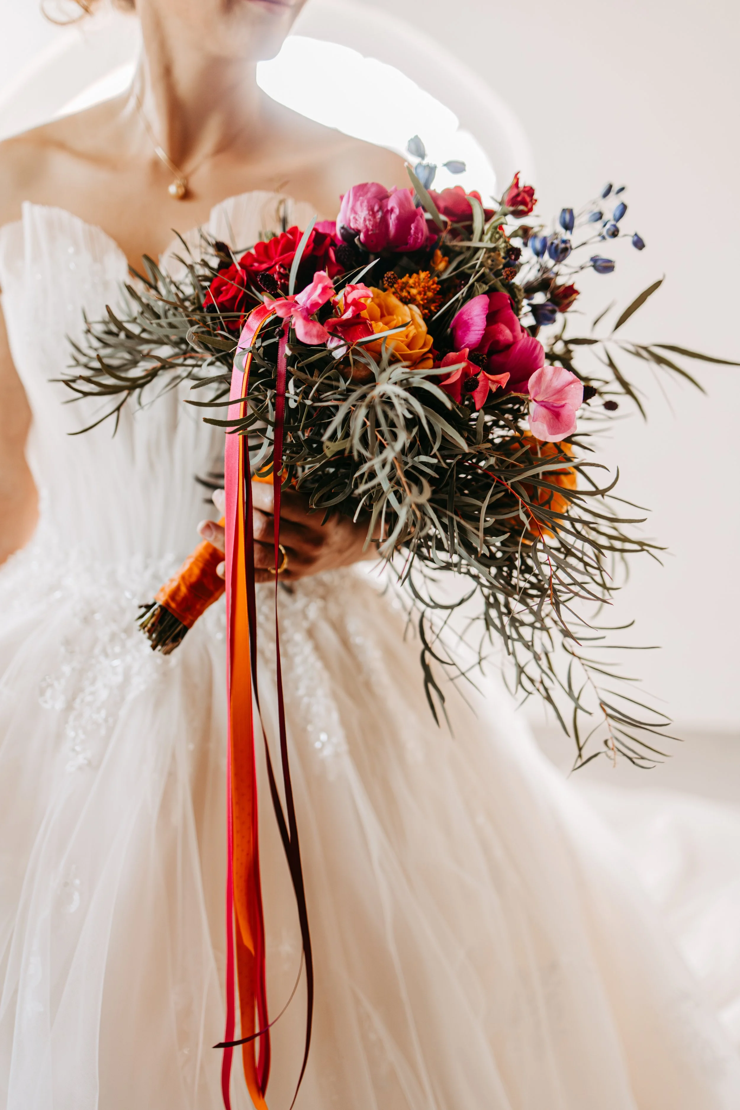 A bride in a wedding dress holding a colorful bouquet of flowers.