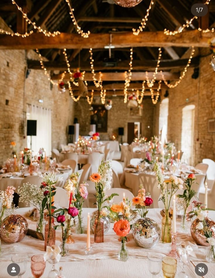 A table decorated with a colorful floral centerpiece, pink napkins, clear glasses, and gold flatware.