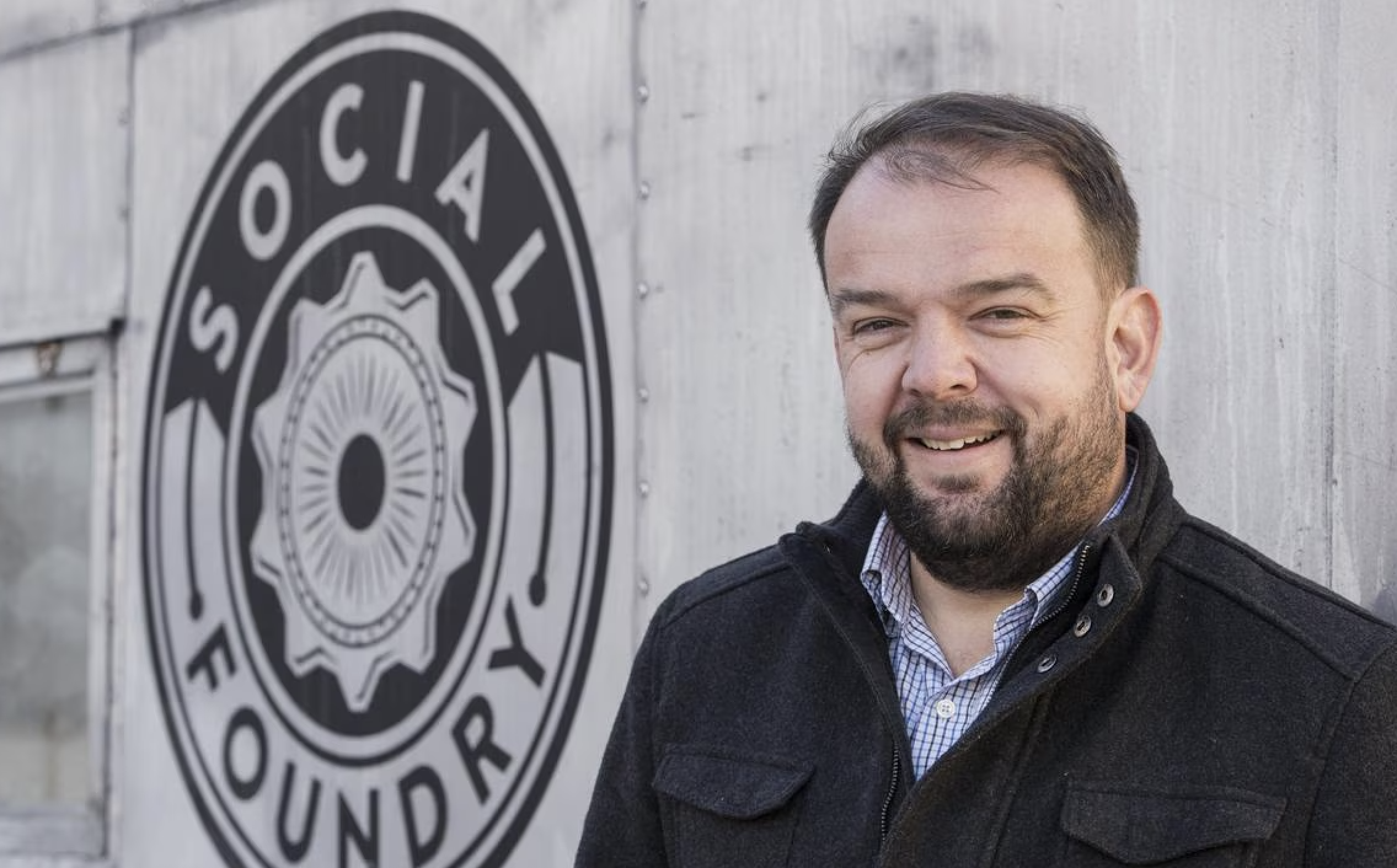 Paul Dettmann smiles in front of Social Foundry building with logo on the wall