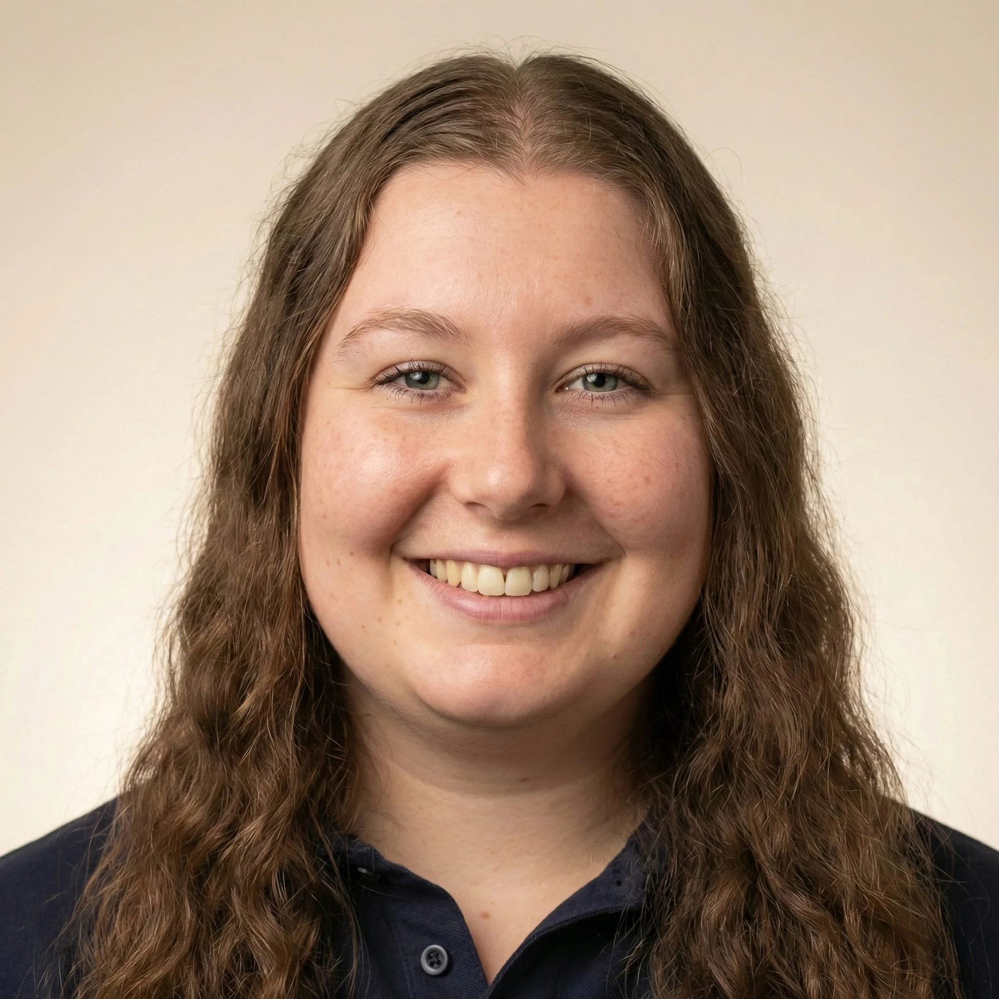 A woman with long, wavy light brown hair smiling, wearing a dark collared shirt against a neutral background.
