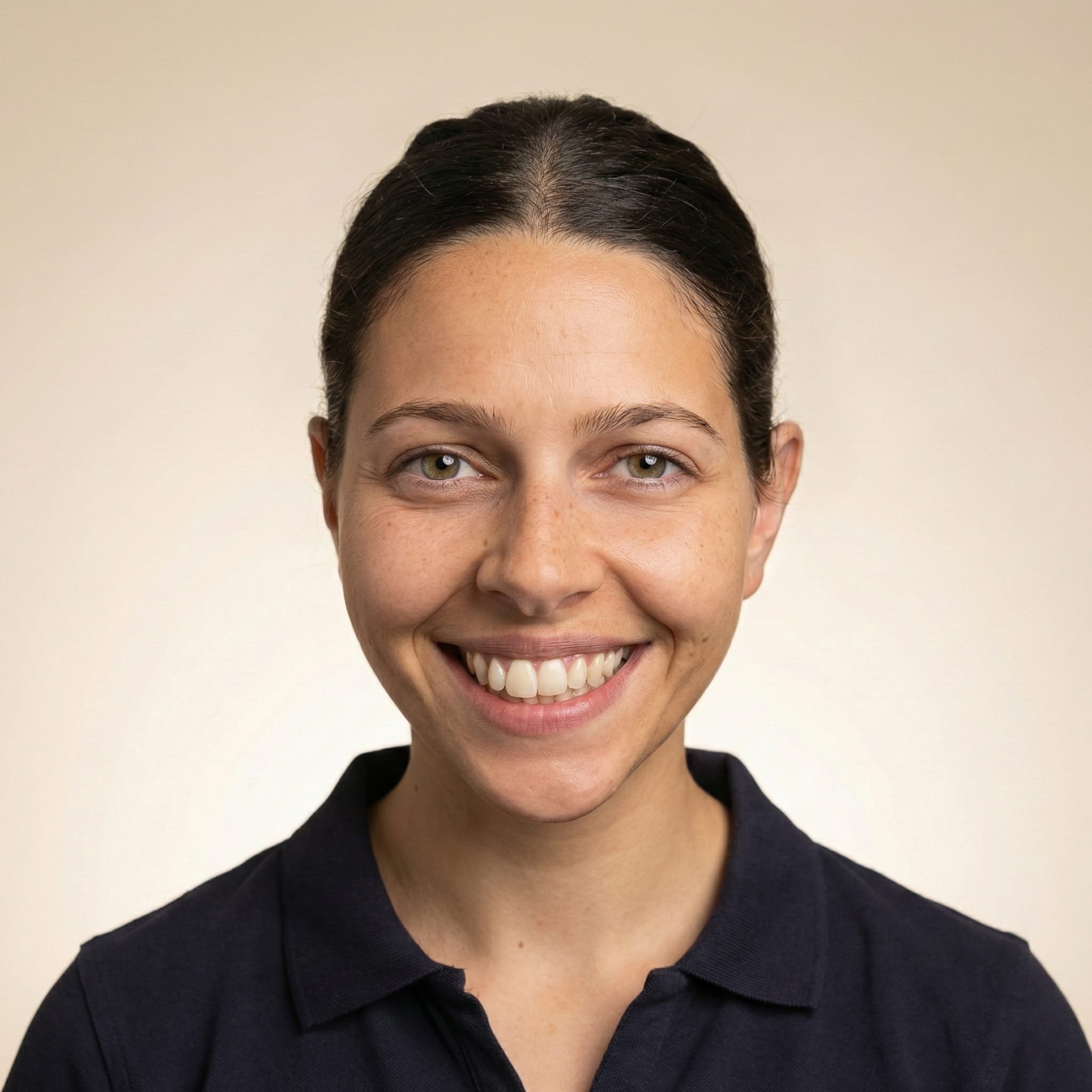 Close-up of a woman with dark hair, smiling, wearing a dark polo shirt, against a plain background.