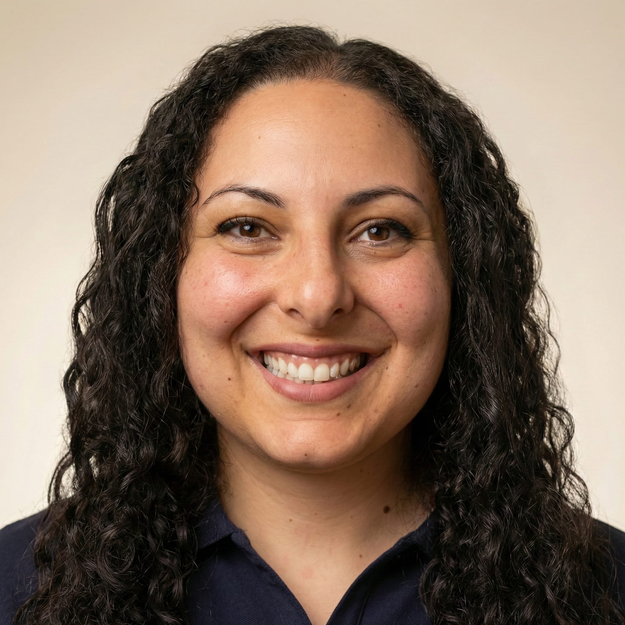 Close-up photo of a smiling woman with curly dark hair, wearing a dark shirt, against a light background.