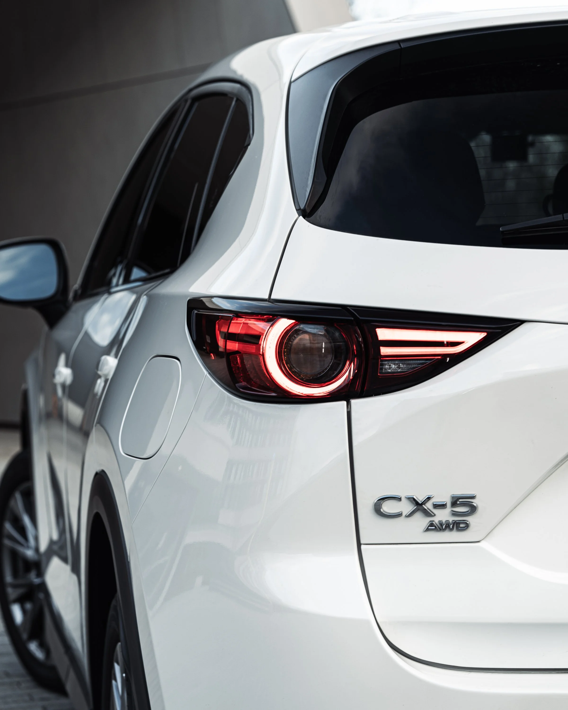 Close-up of the rear side of a white Lexus CX-5 AWD SUV, showing tail light and part of the rear window.