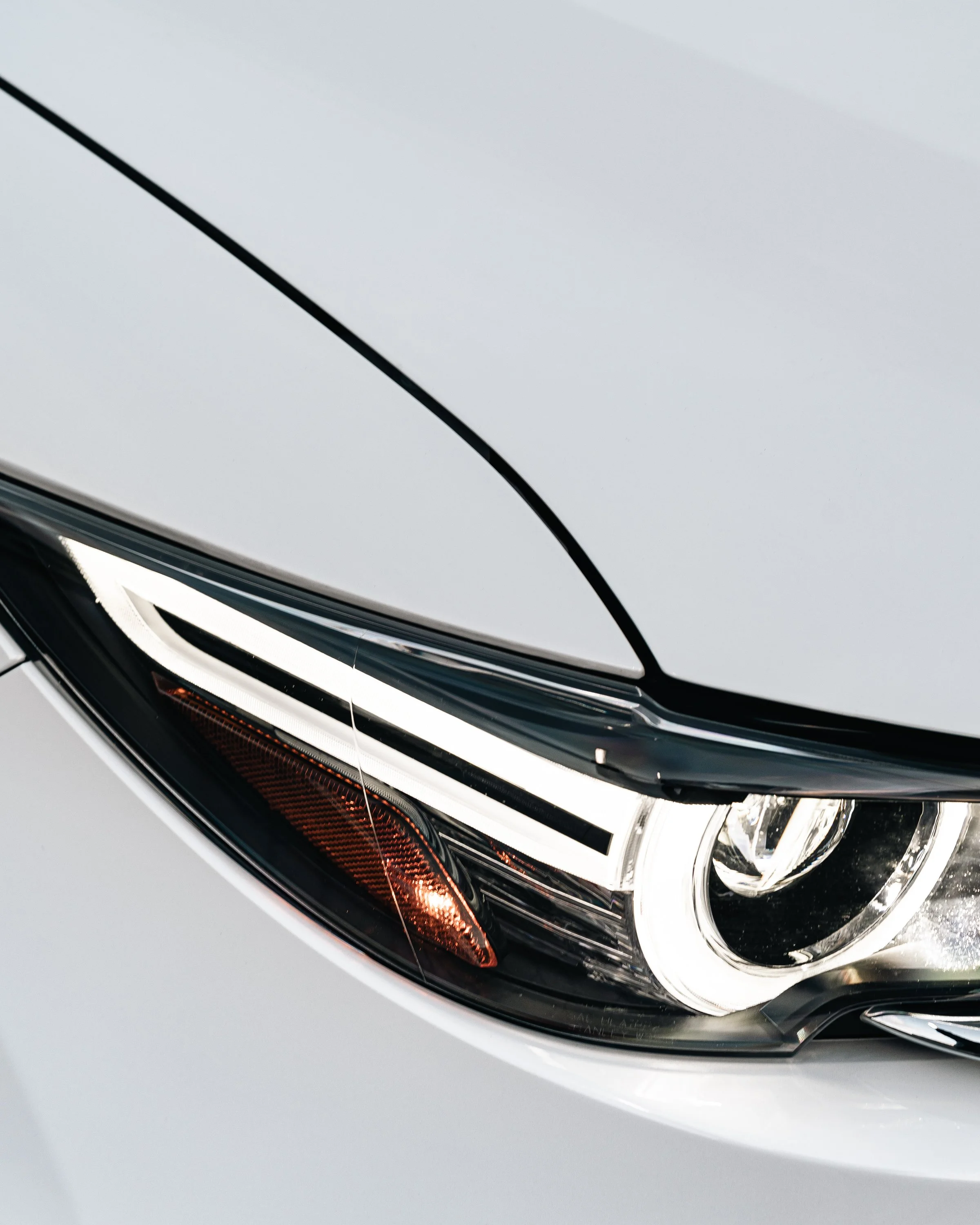 Close-up of a modern car's headlight with intricate design, sharp lines, and a mix of black, silver, and clear elements.