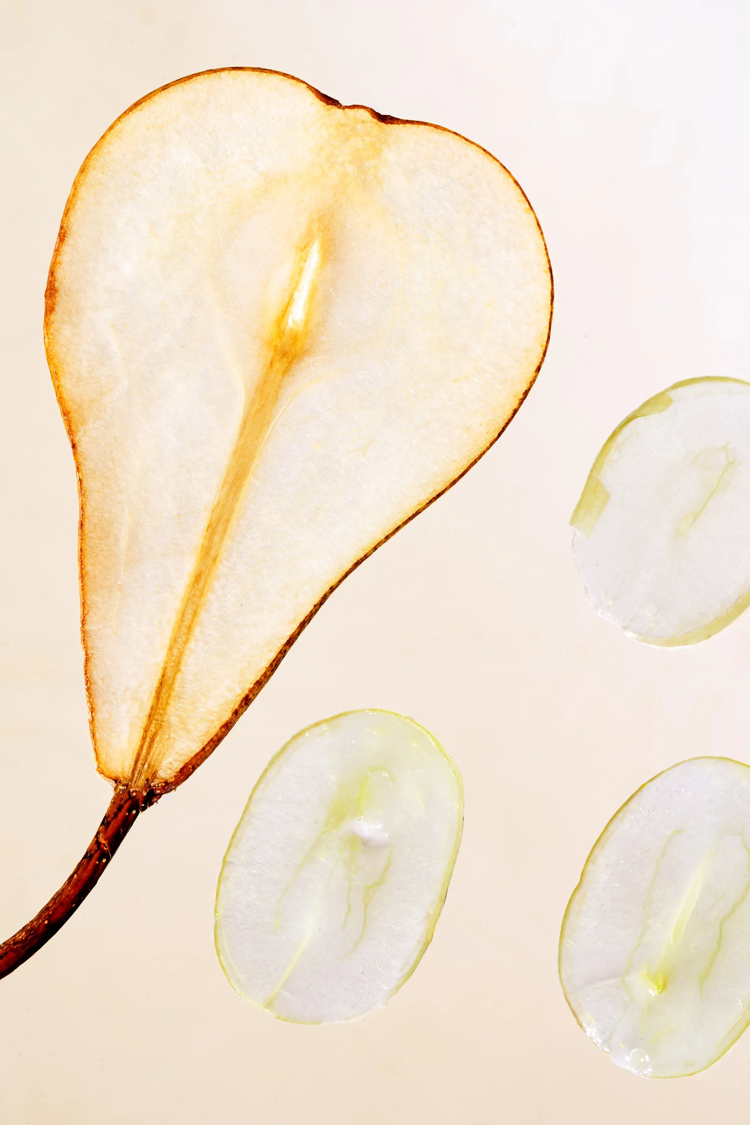 A sliced pear and several thin slices of grapes arranged on a white surface.
