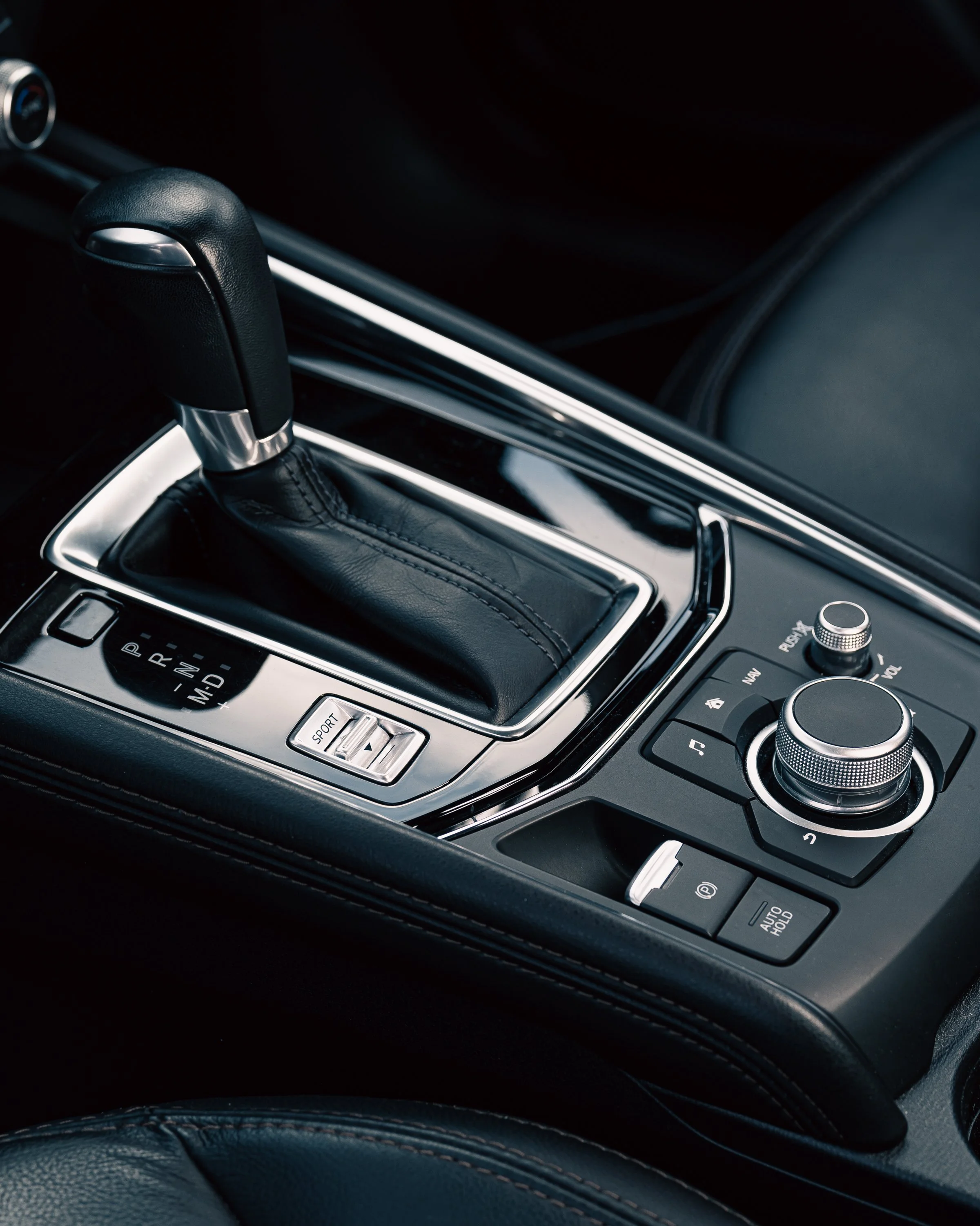 Close-up view of a car's gear shift levers and surrounding control panel, with a leather surface in the foreground.