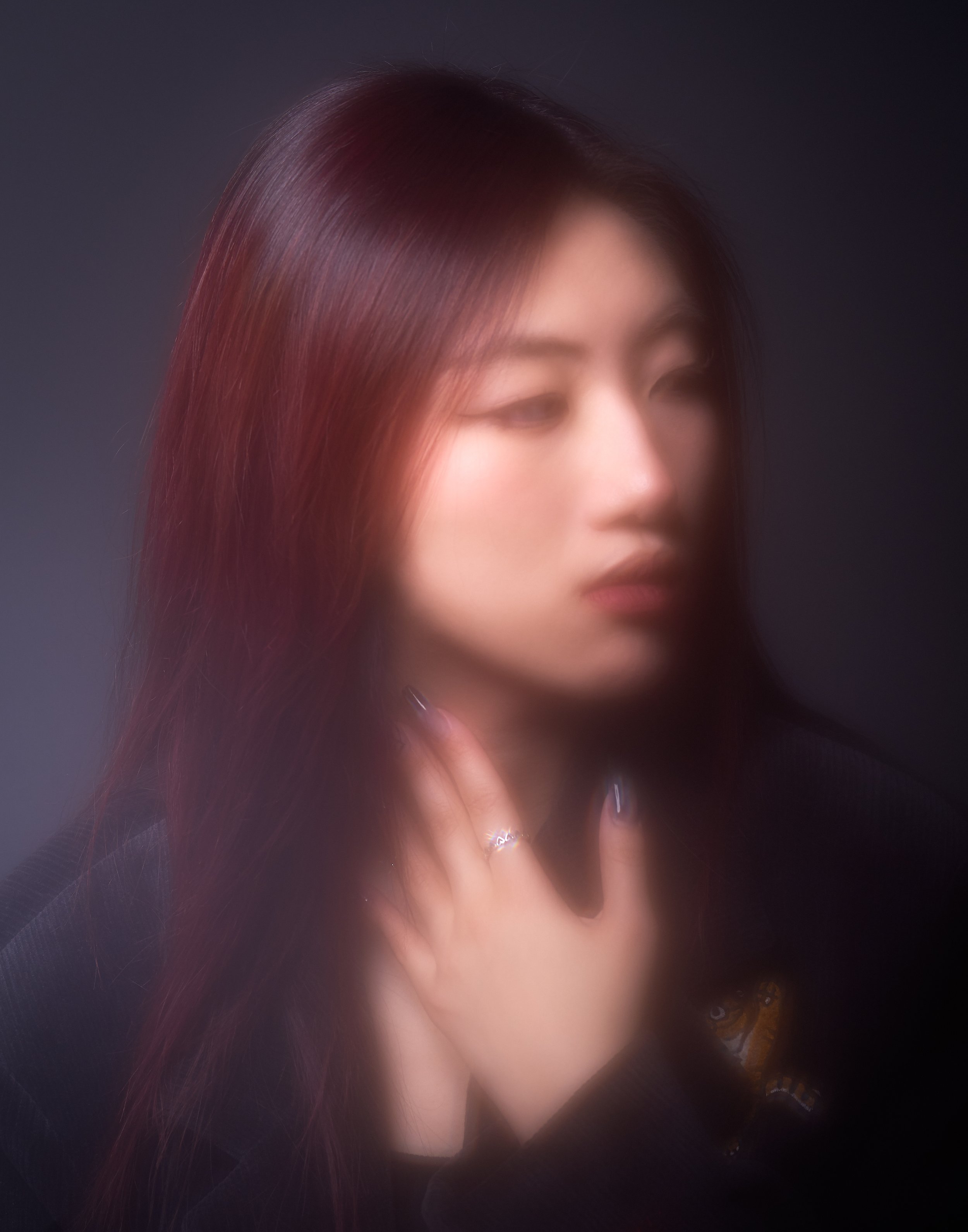 Close-up of a woman with long dark red hair, partially covering her face, with a blurred background.