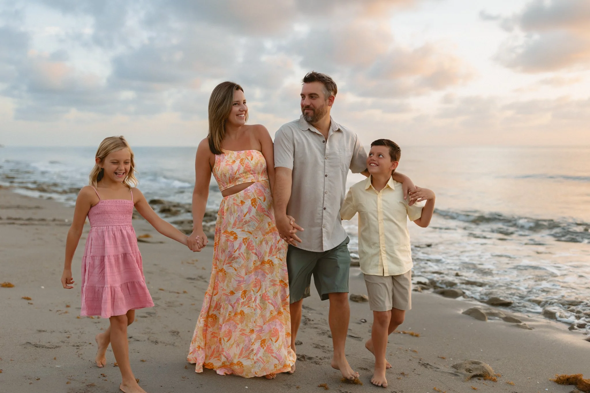 Family walking hand-in-hand along the beach during sunset, smiling and enjoying the moment.