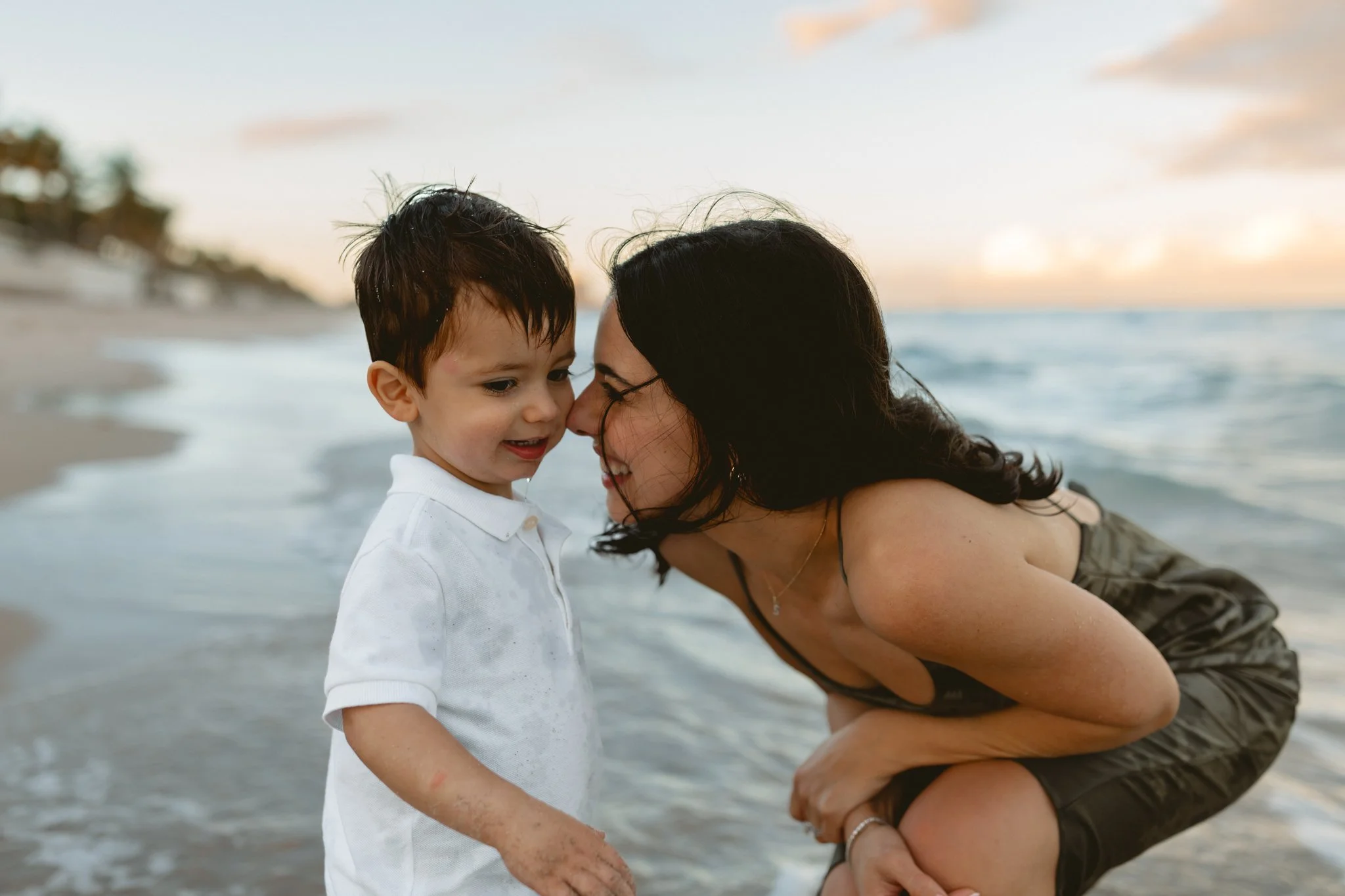 mother in a green dress giving her child kisses on the beach