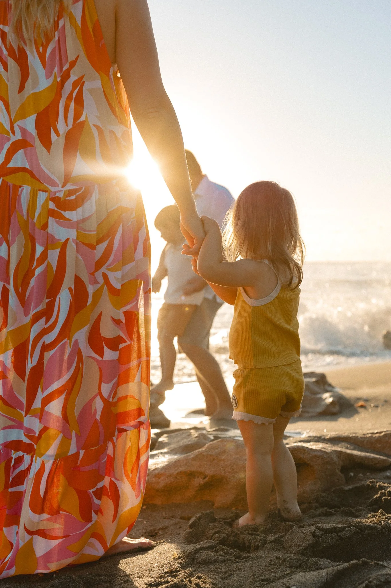 a mother and daughter holding hands on the beach with the sun shining through 