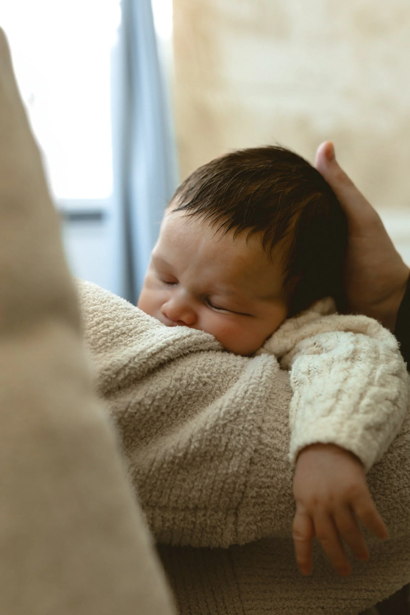 A sleeping baby being held gently in someone's arms, with the person's hand supporting the baby's head.