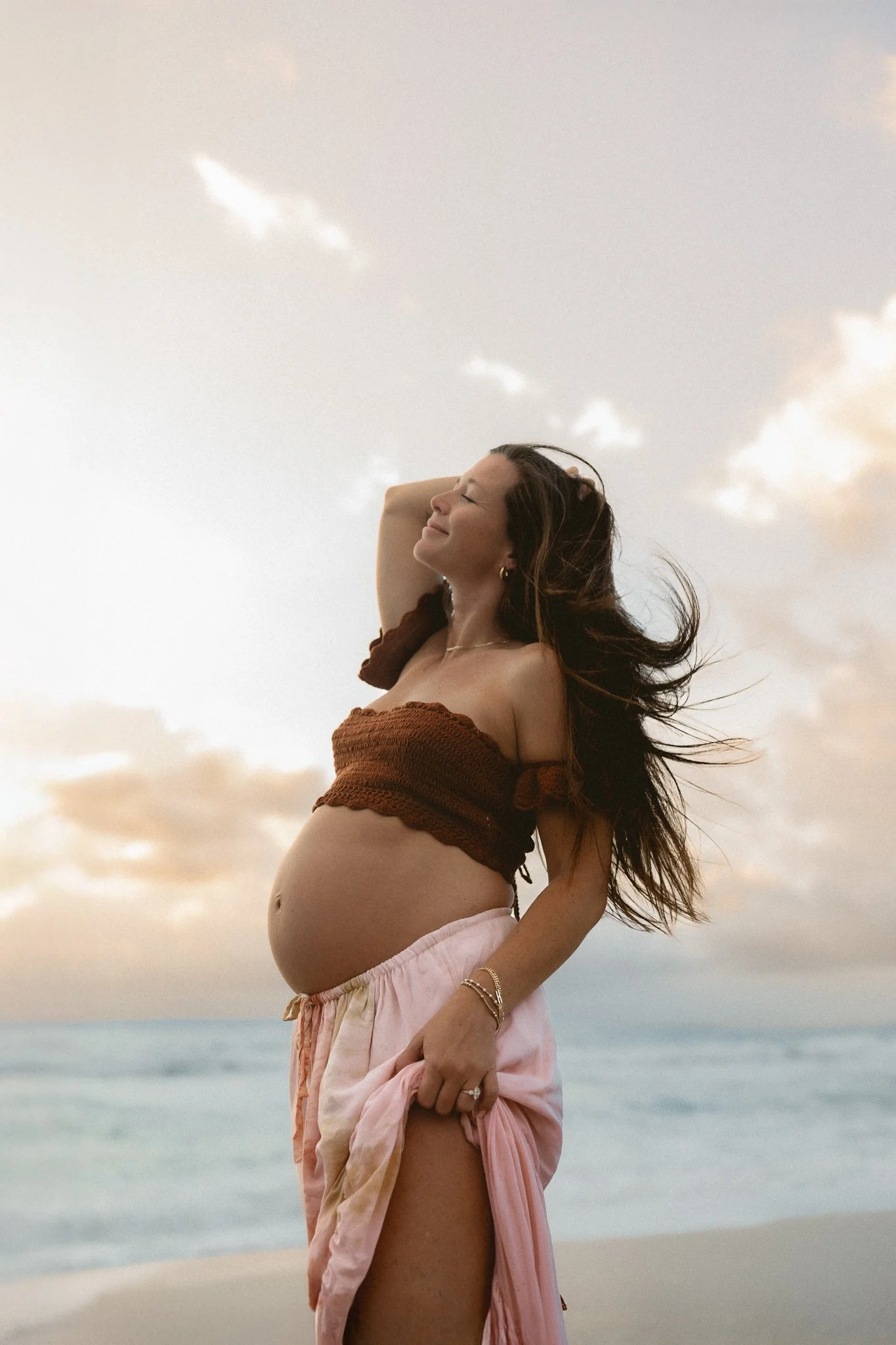 pregnant woman shaking her hair with her hand on a beach during sunrise