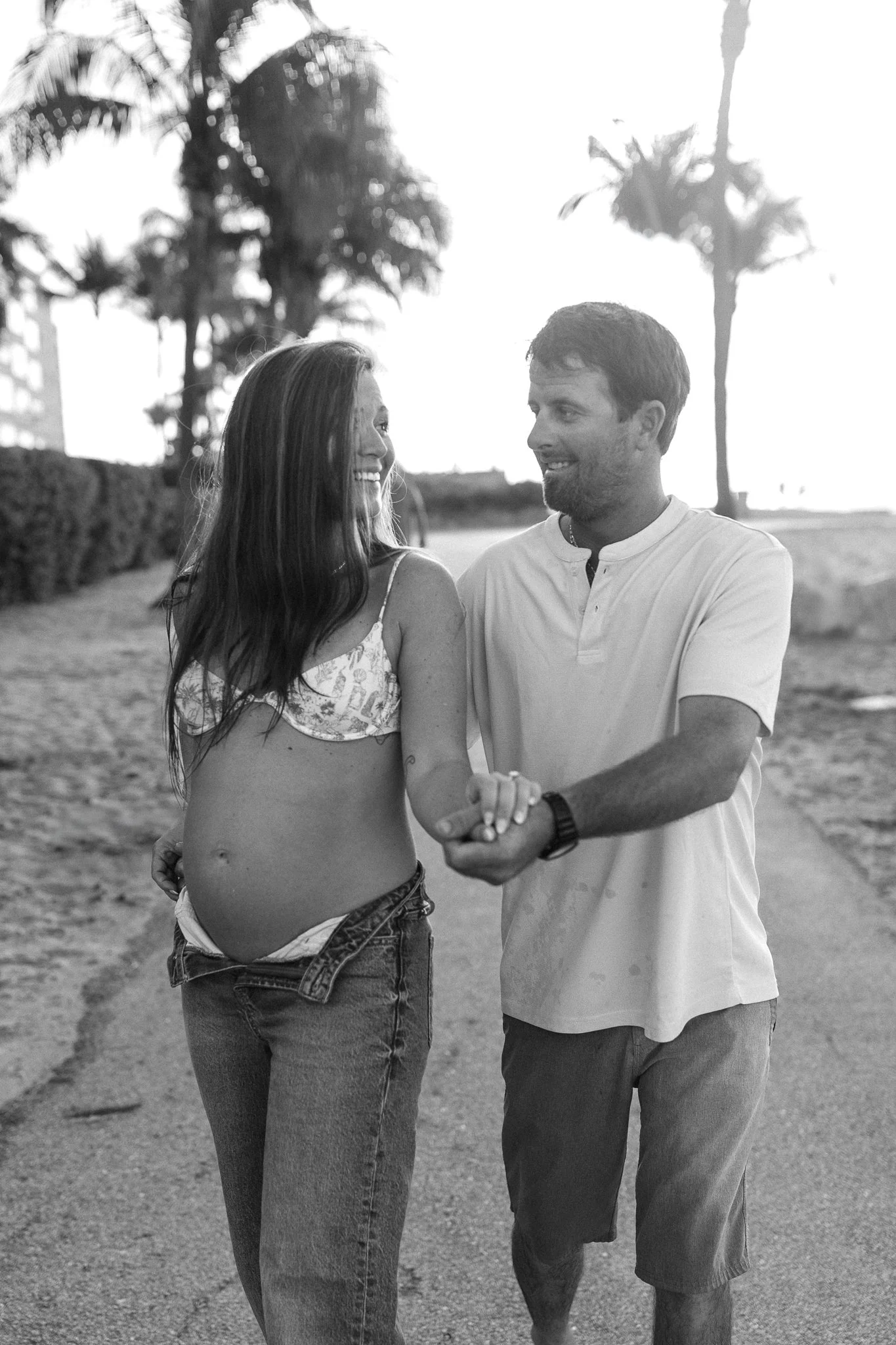 pregnant woman riding a skateboard while holding hands with her husband