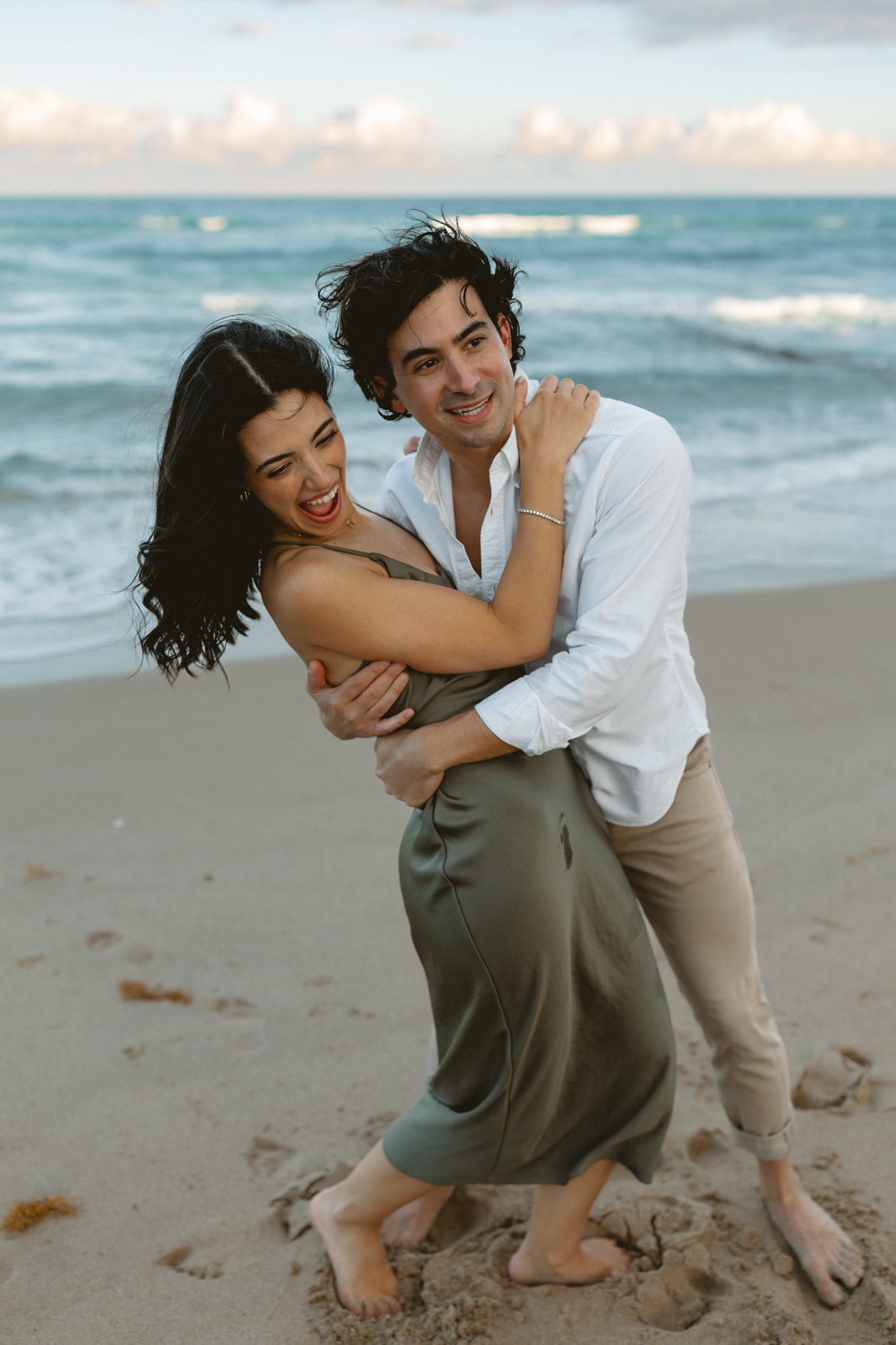 a young mother and father embracing each other on the beach during sunset
