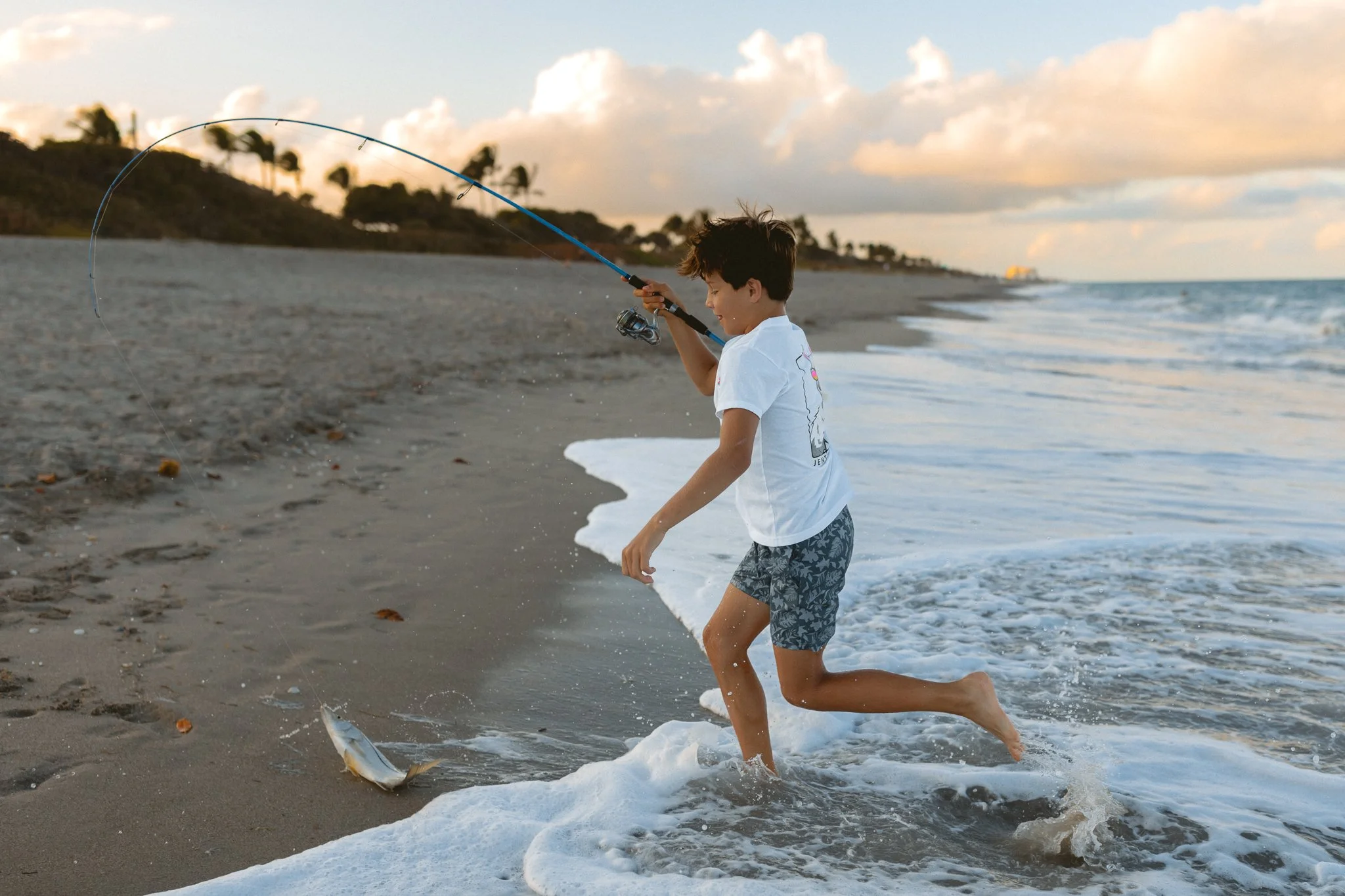 a young boy running up the beach with a snook caught on his fishing pole