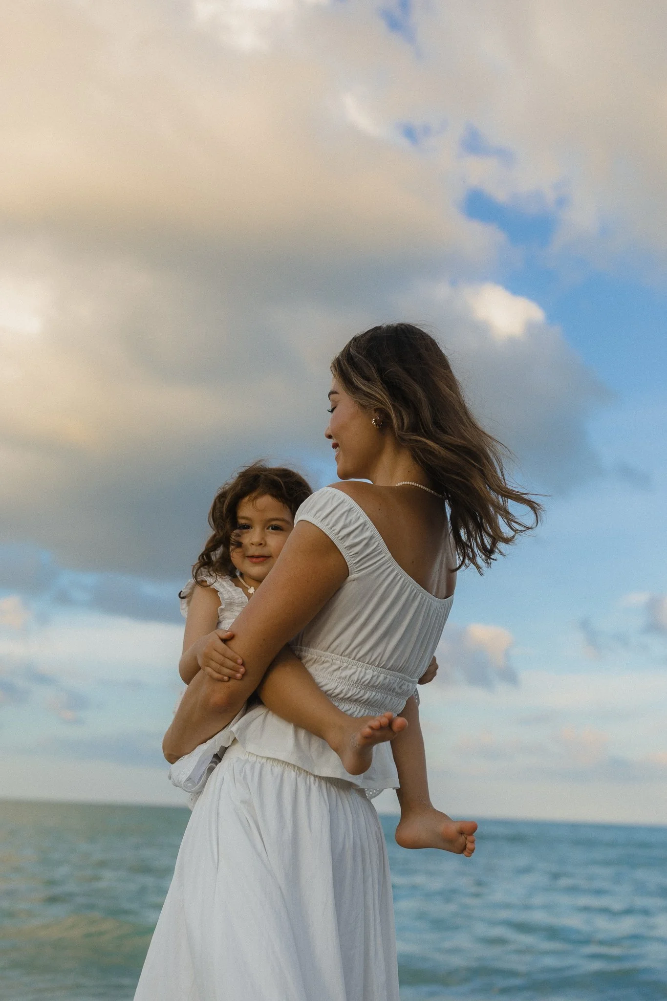 Woman spinning her young daughter on the beach during golden hour