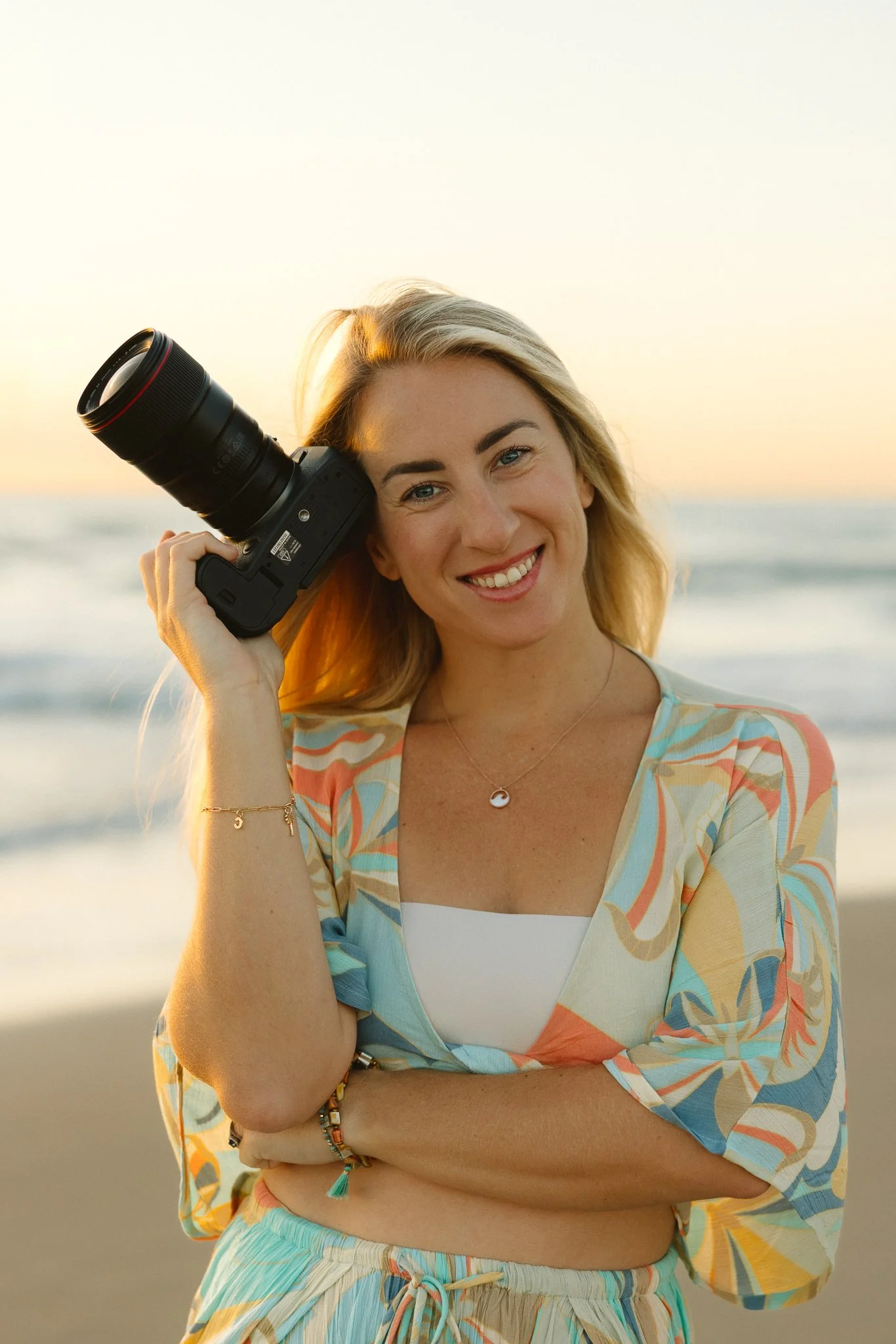 woman holding a camera close to her head on the beach