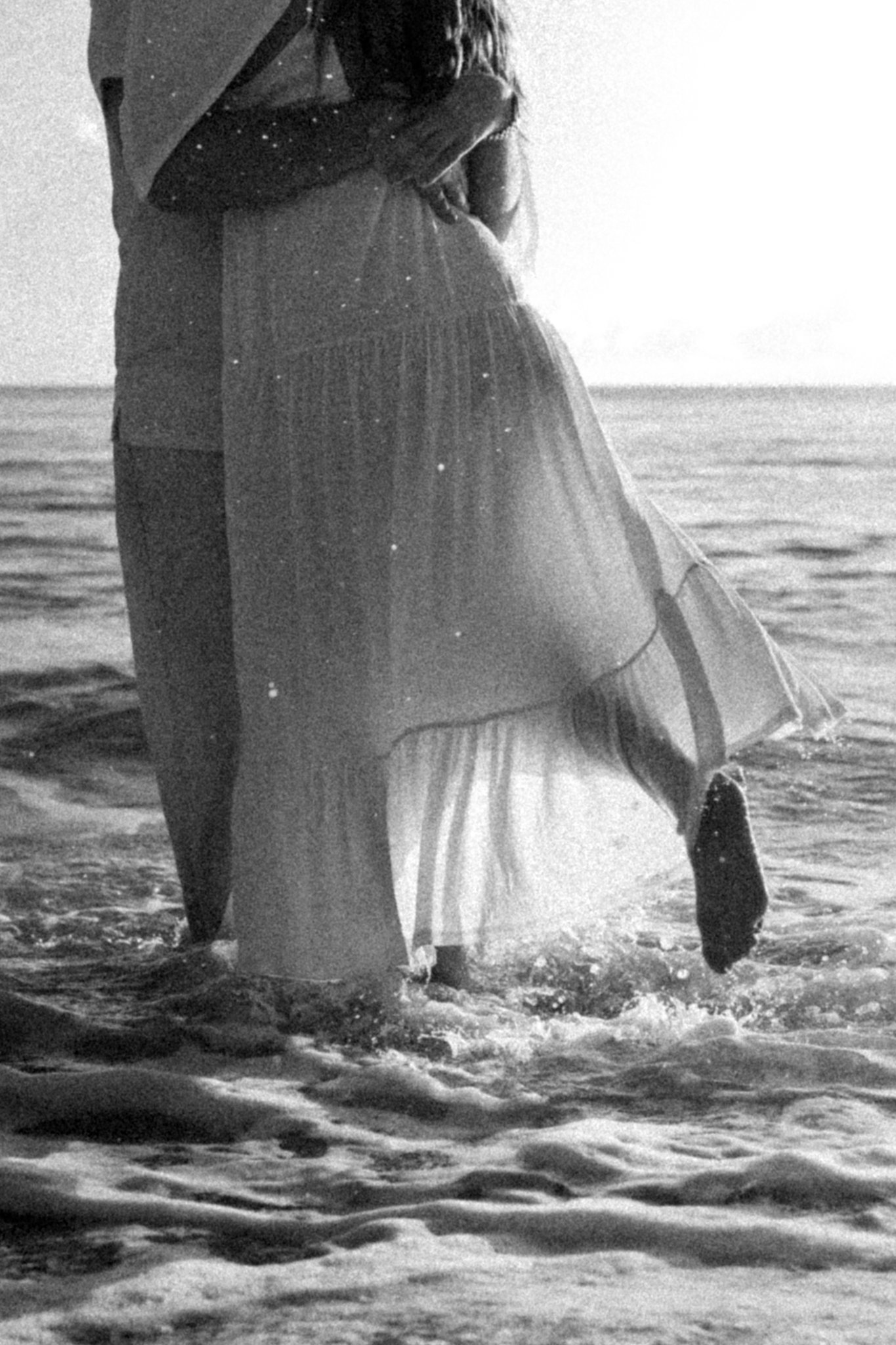 A person holding a child on the beach with the ocean in the background, black and white photo.
