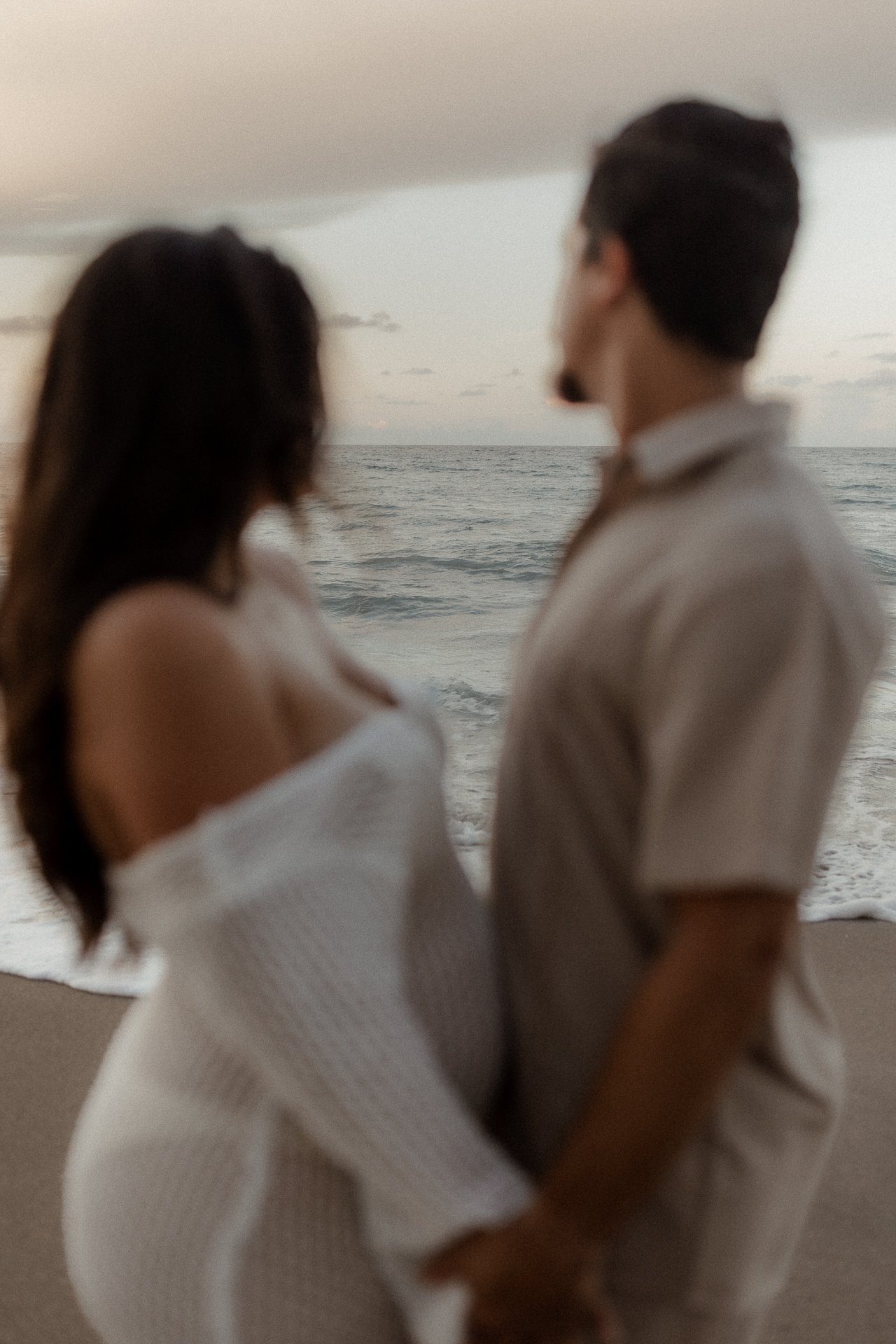 A romantic couple gazing at the ocean during sunset on a beach.