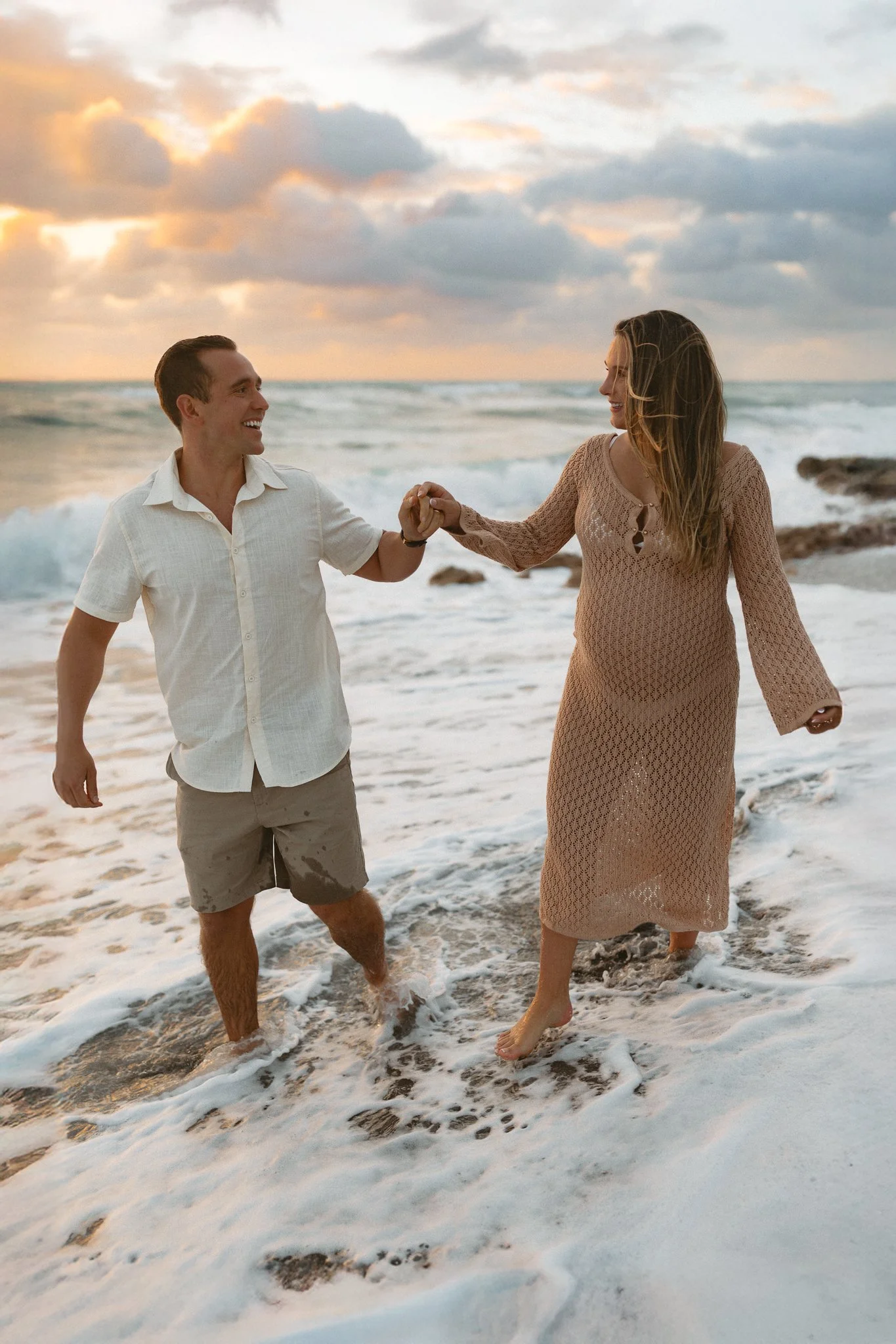 Pregnatn woman holding hands with her husband on the beach at sunrise