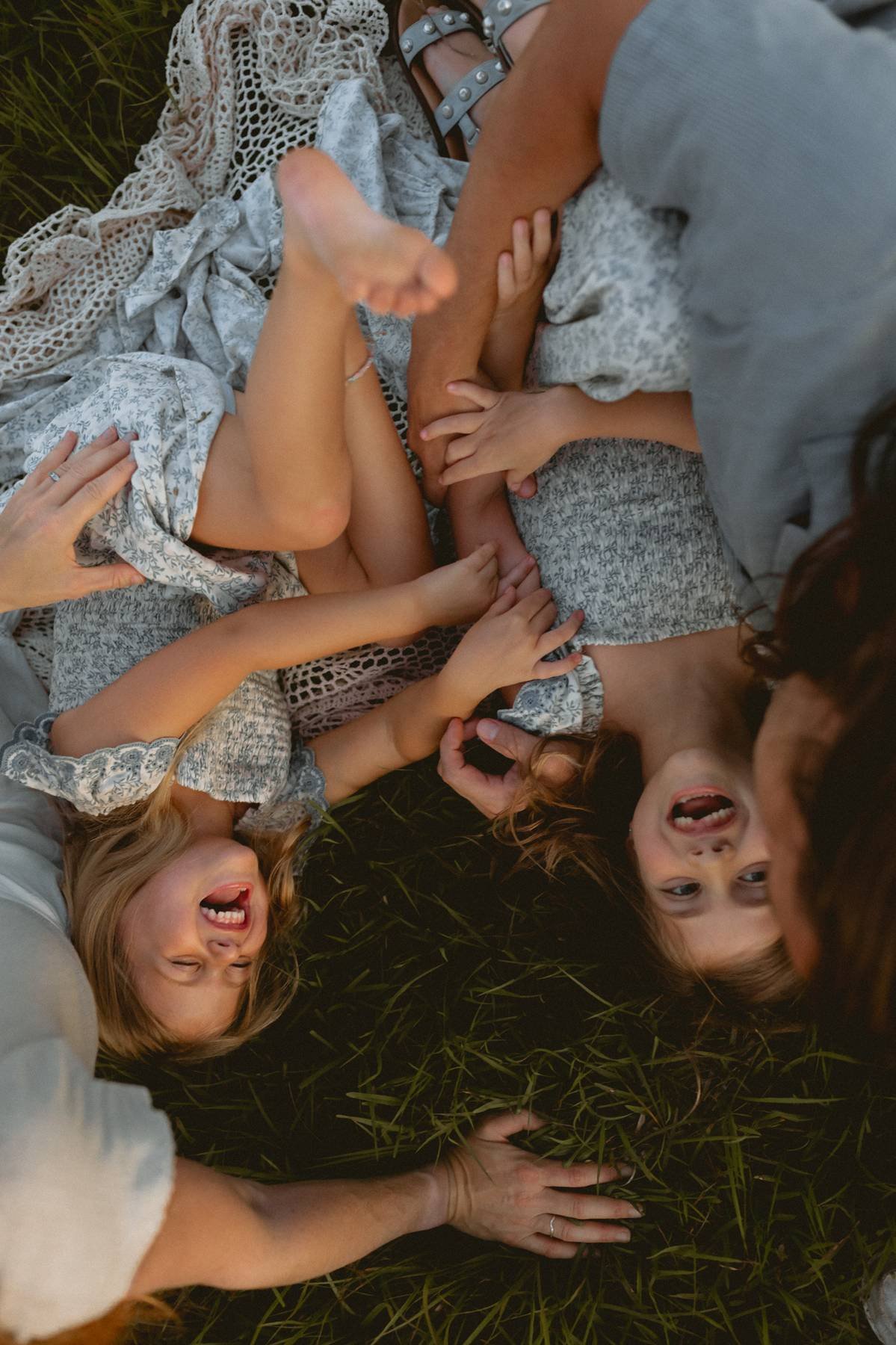 Two women and three children lying on grass, smiling and playing together.