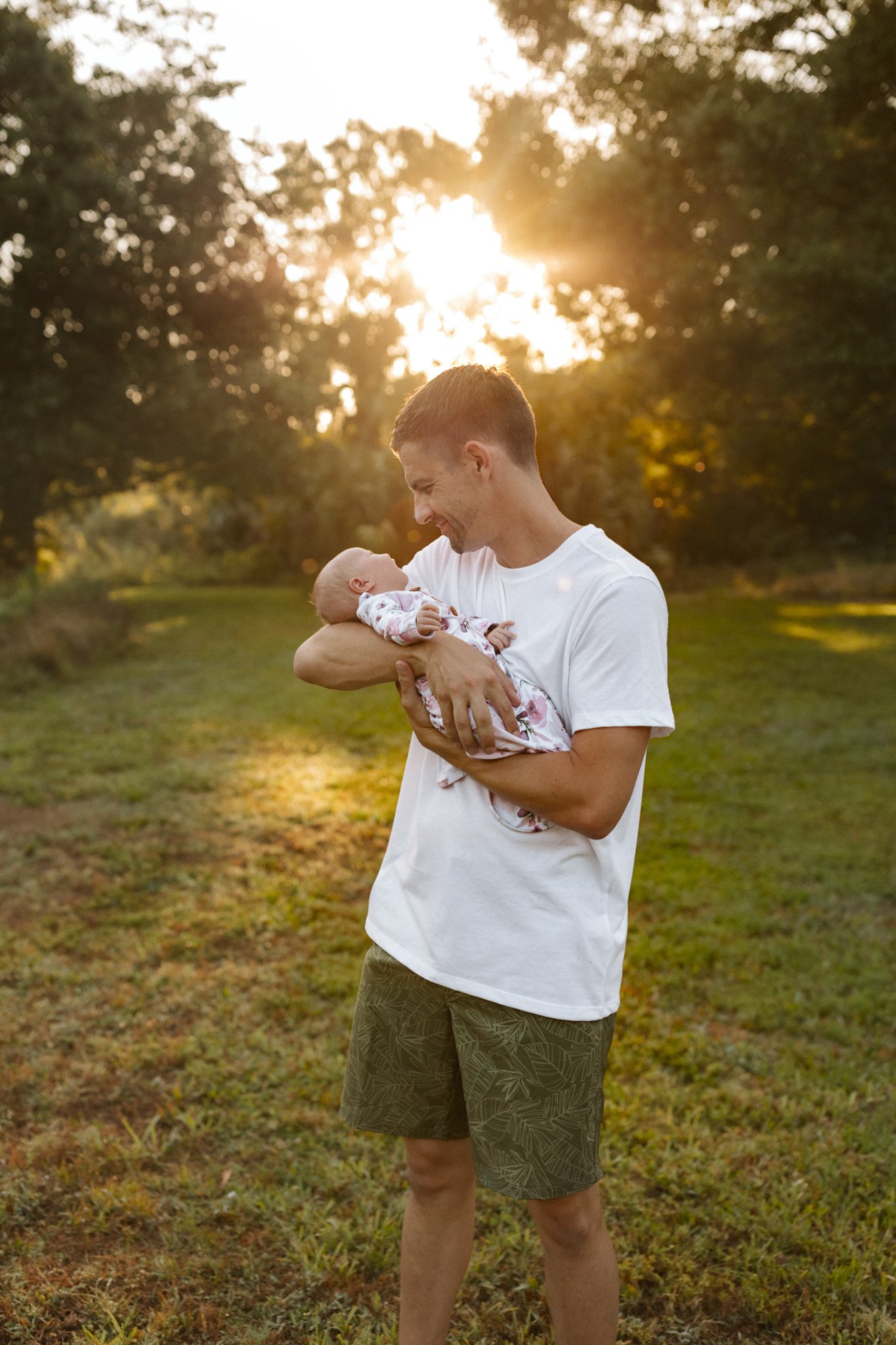 A man holding a baby girl outdoors during sunset, smiling at each other.