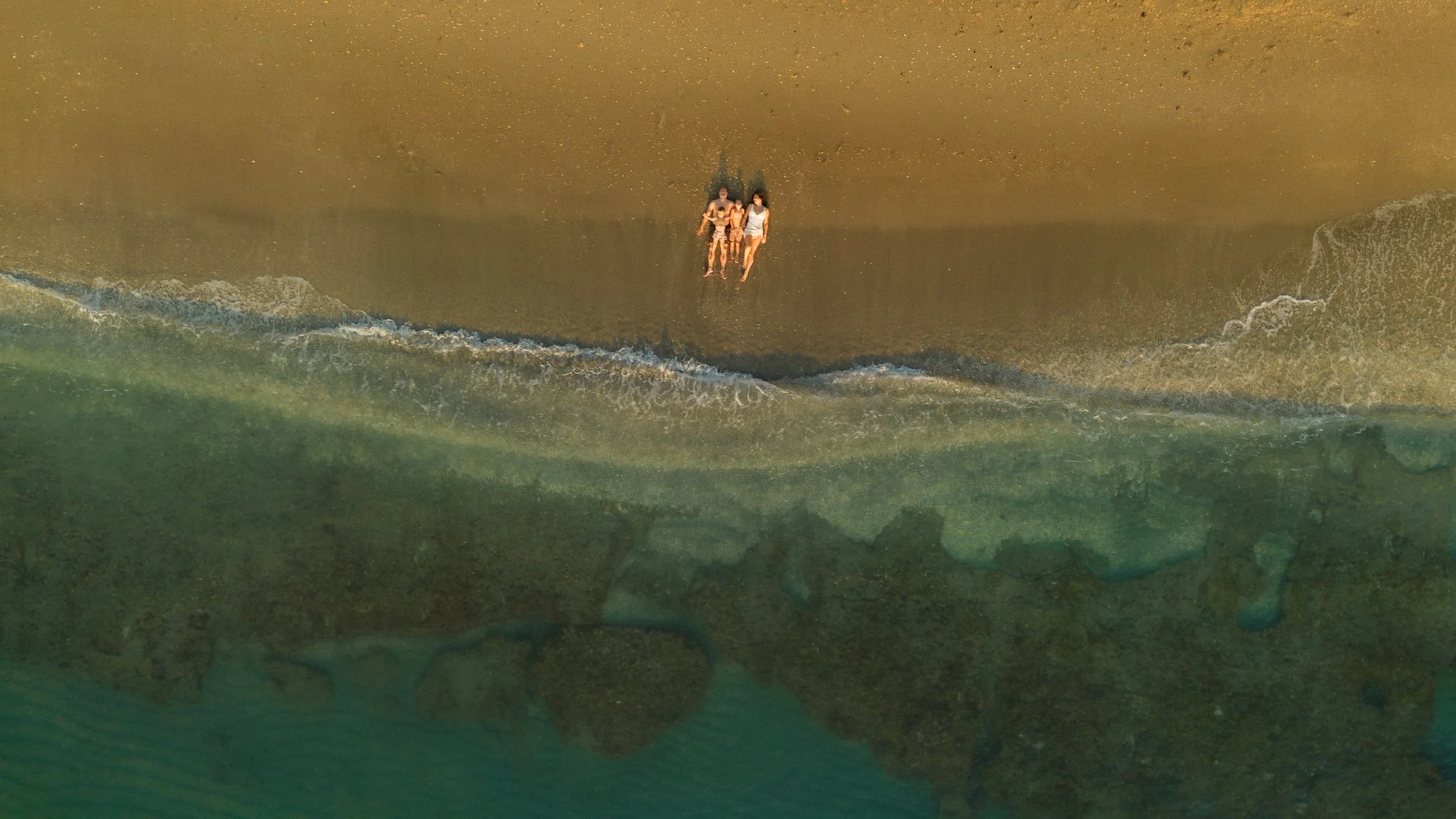 drone image of a family laying on the shore of a beach at sunrise