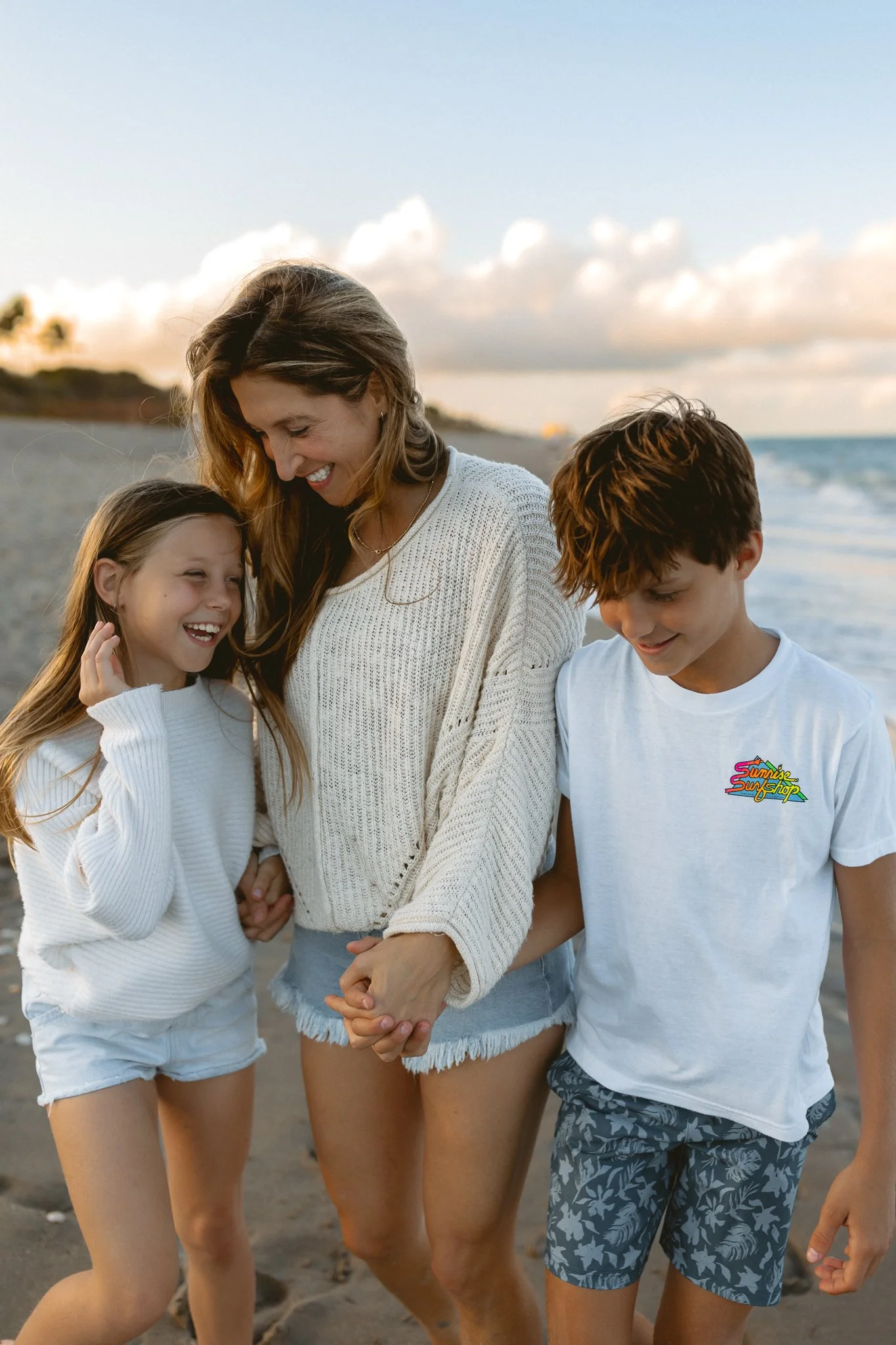a mother with her young son and daughter walking down the beach during golden hour