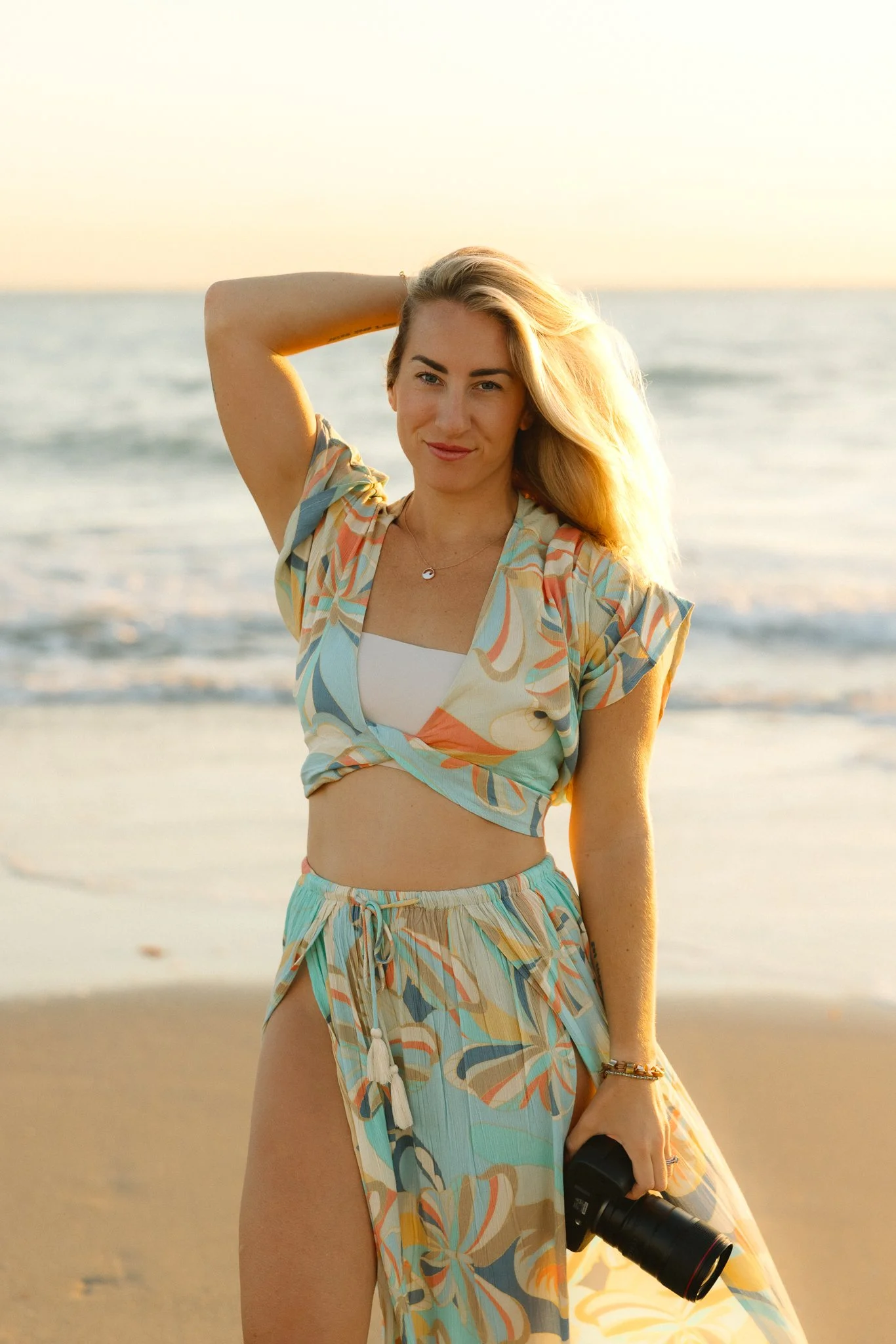 Young woman standing on the beach at sunrise holding a camera
