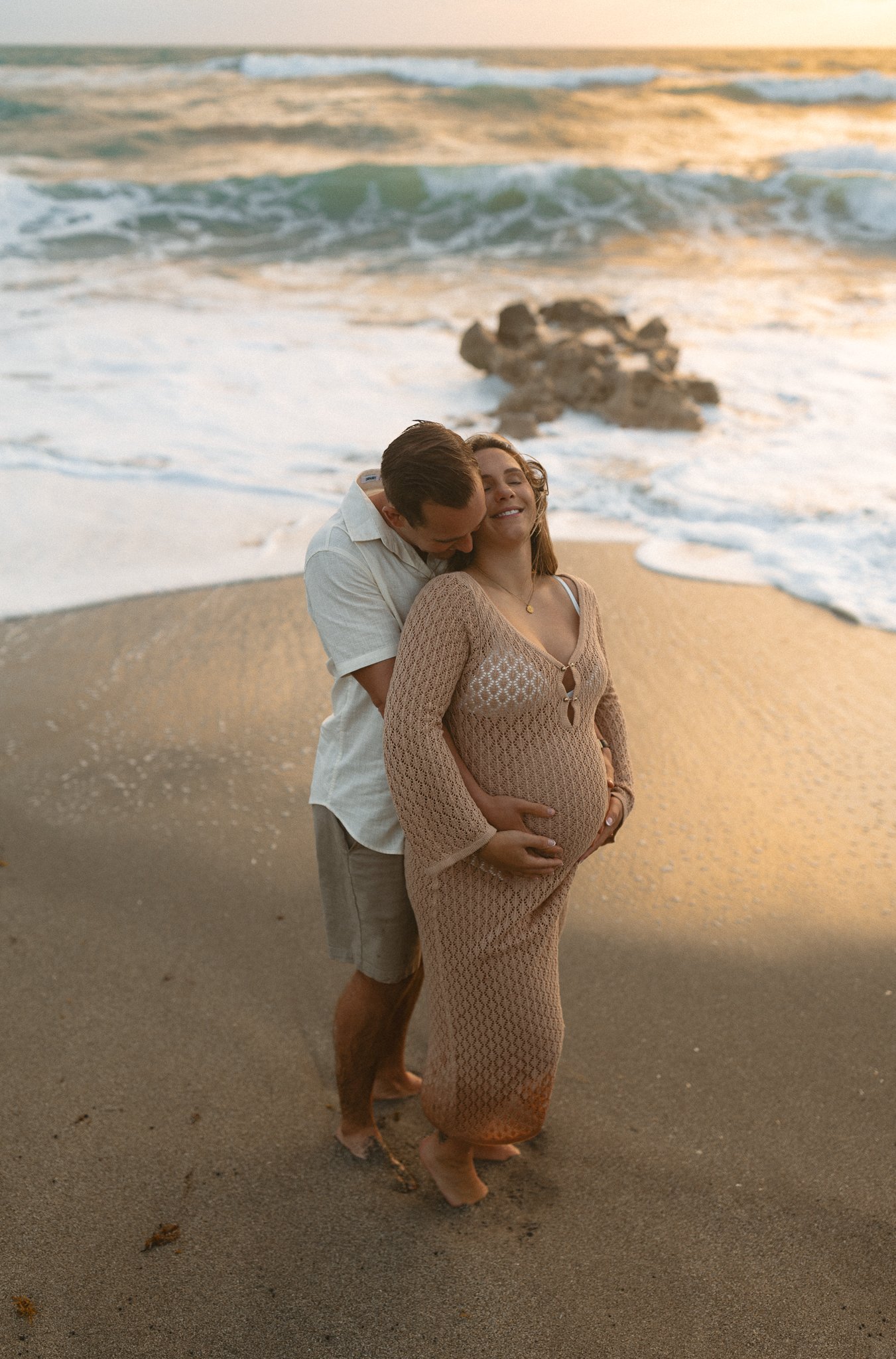 pregnant woman held tightly by her husband on the beach