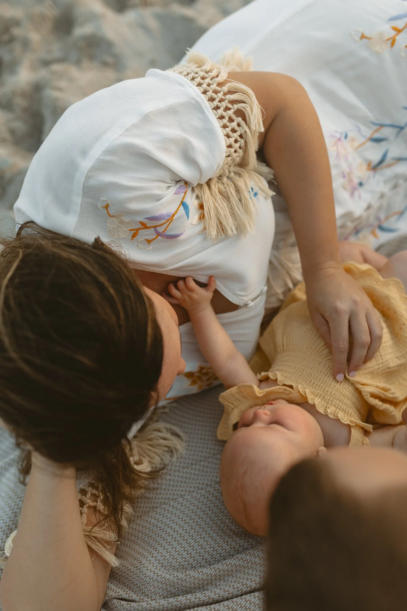 a mom and baby laying down on a beach blanket with the baby reaching up towards her