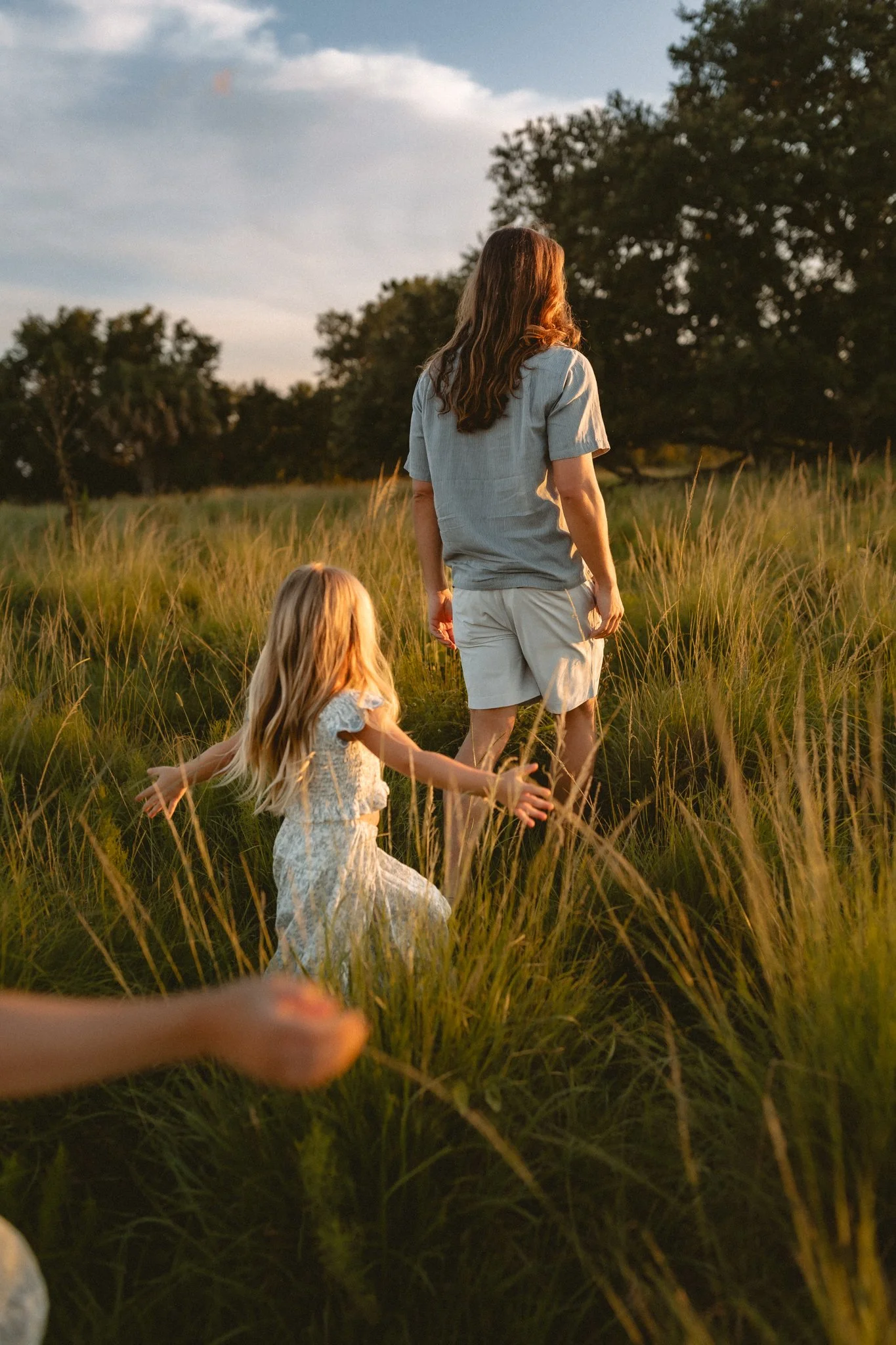 A woman and a young girl walking through tall grass during sunset.