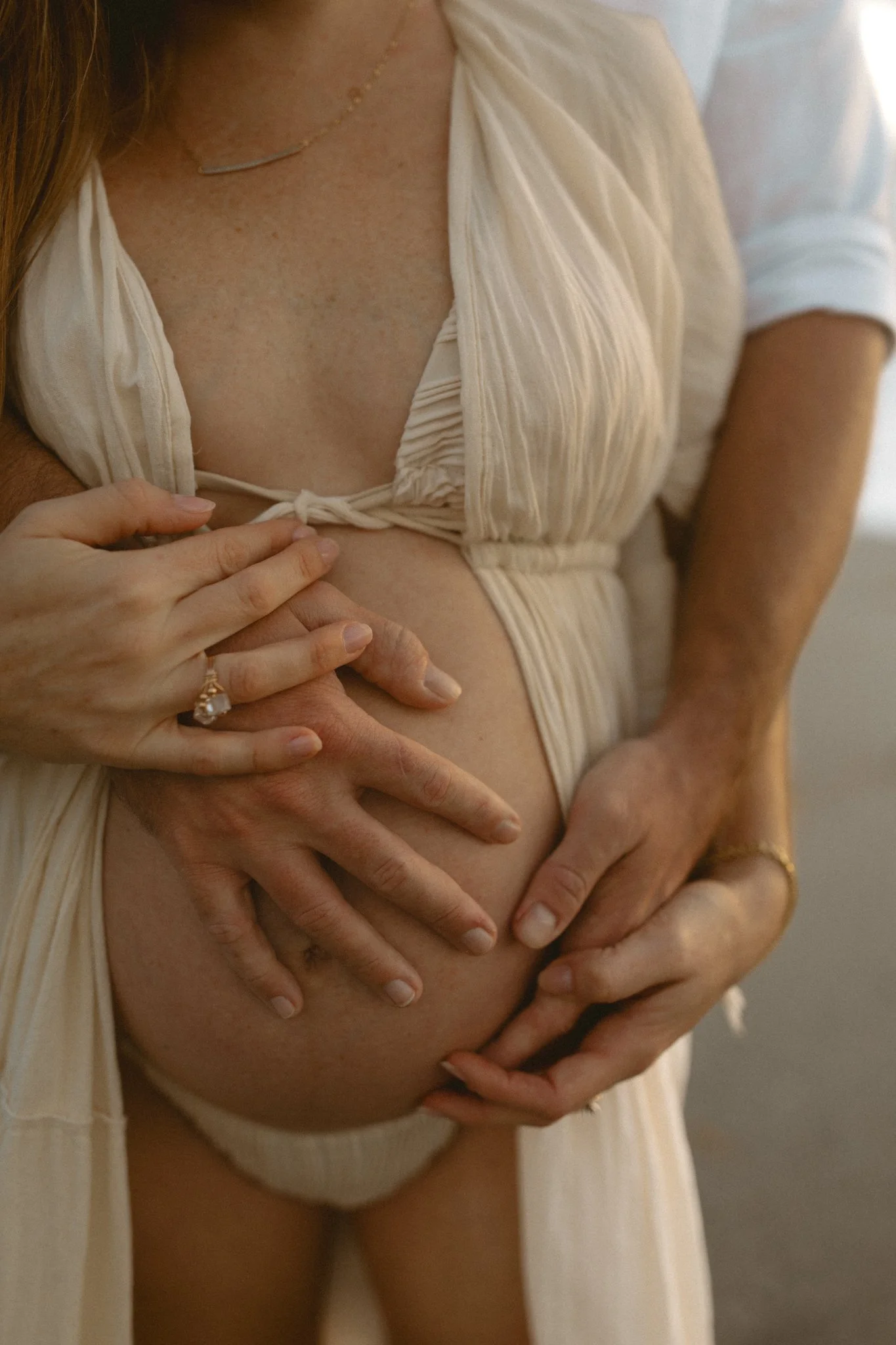 Close-up of a pregnant woman and her partner showing their hands on her belly during pregnancy, with the woman wearing a ring and a ringed hand touching her stomach.