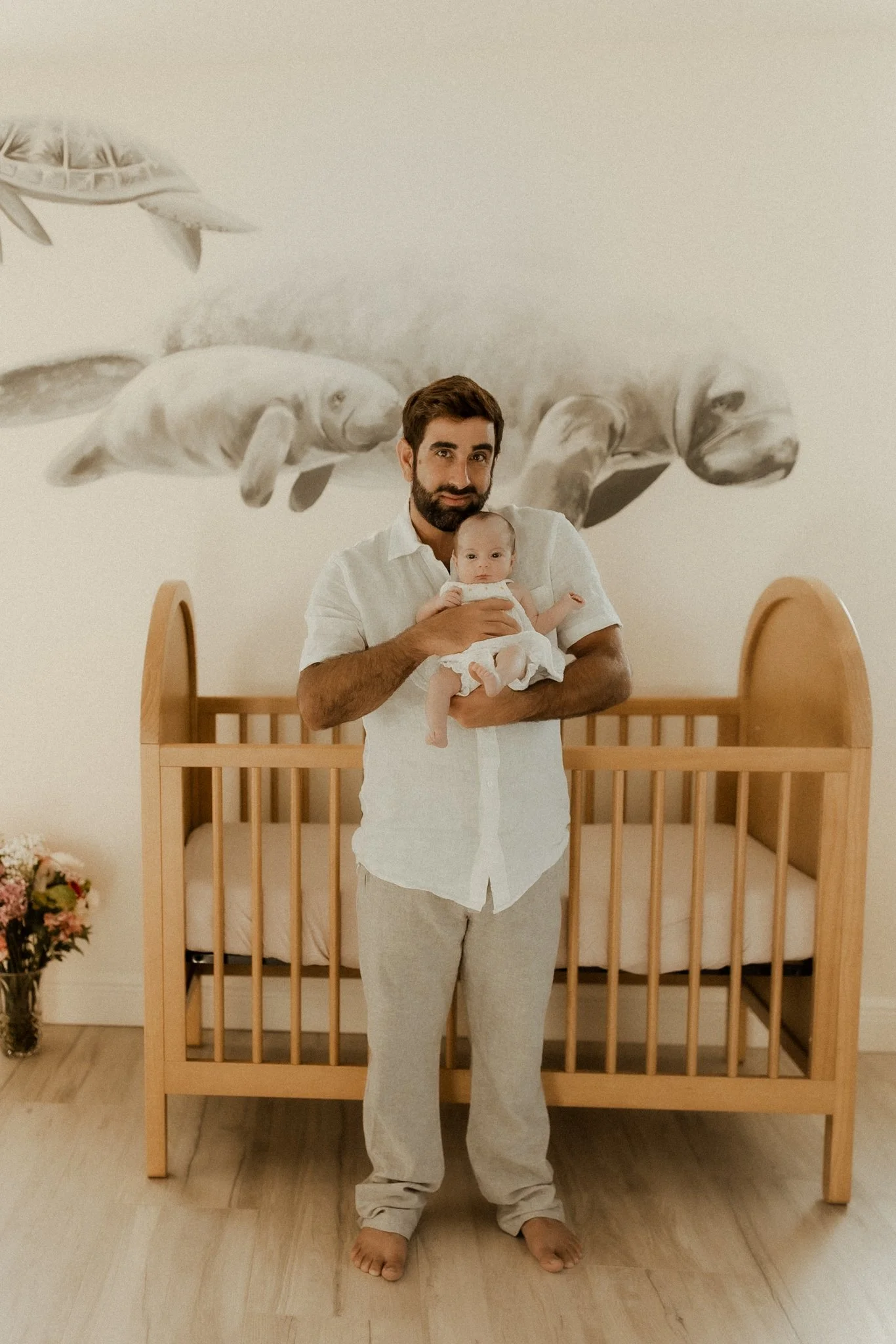 Man holding a baby in a nursery with a whale and fish mural on the wall behind them.