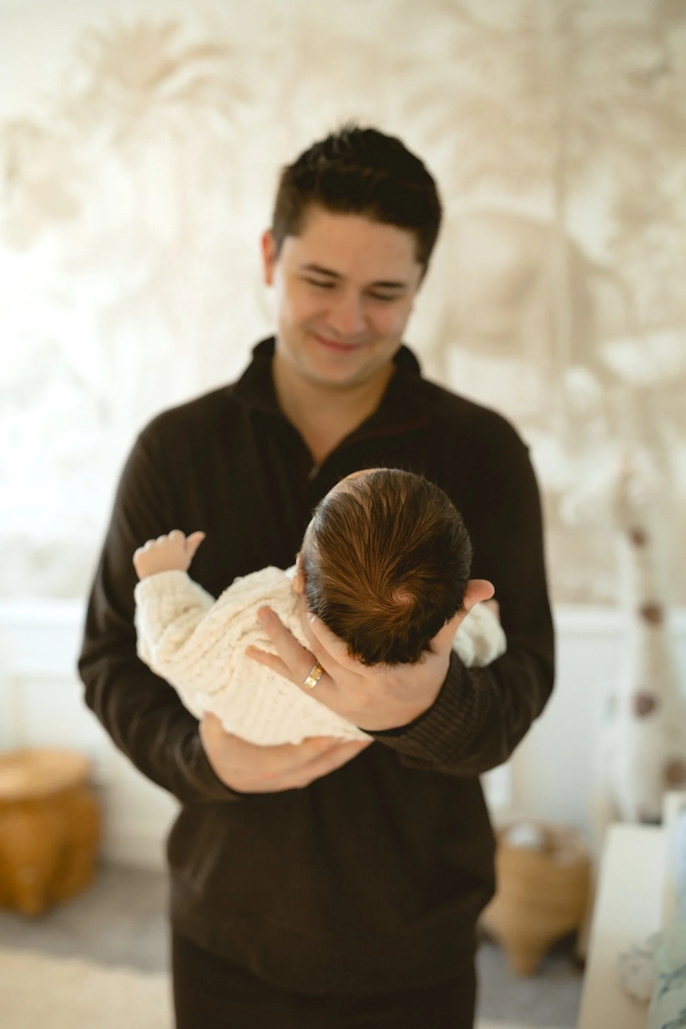 A man is holding a newborn baby in his hands while smiling and looking at the baby.