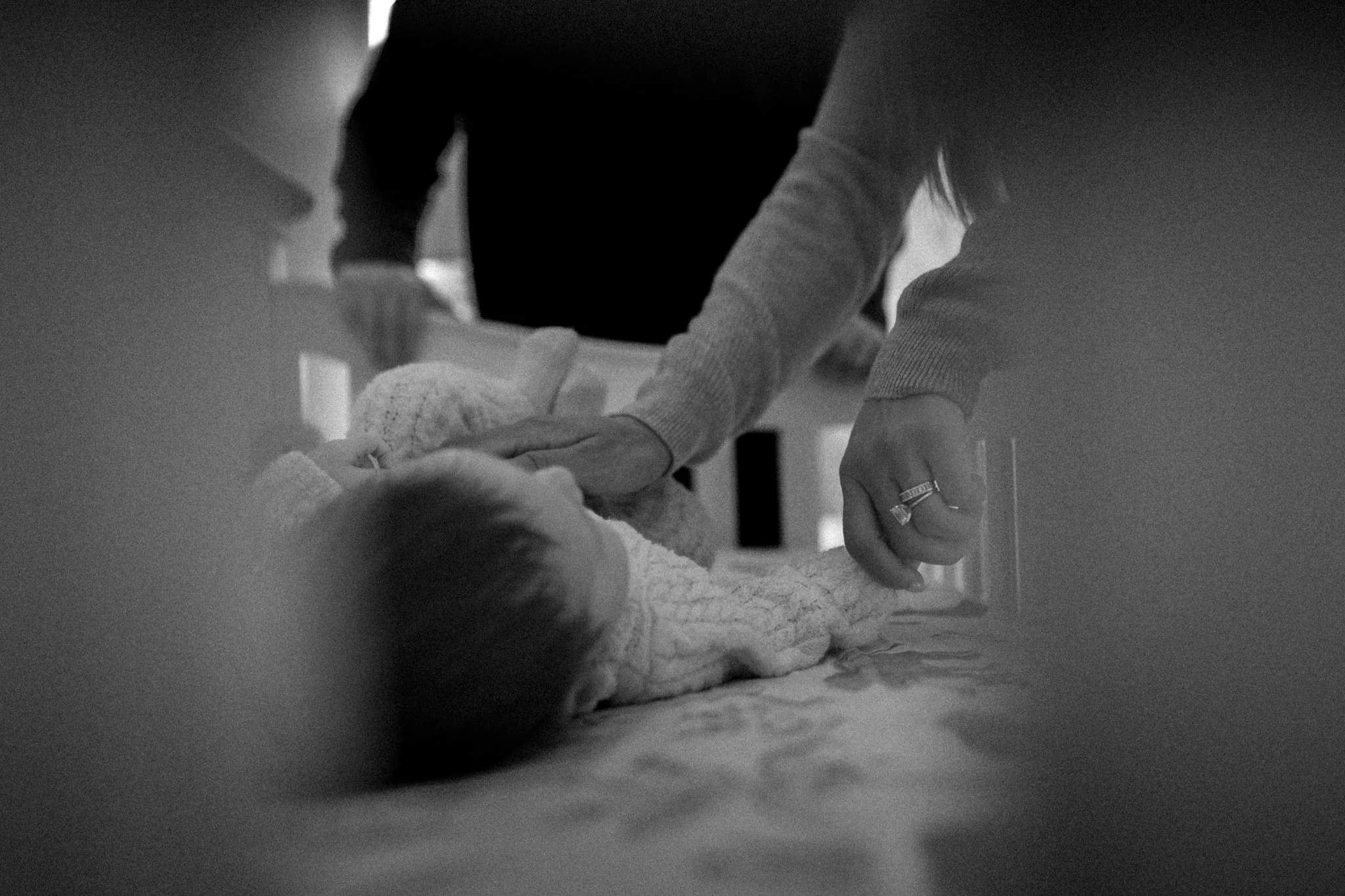 A person leaning over a sleeping baby on a bed, with another person partially visible in the background.
