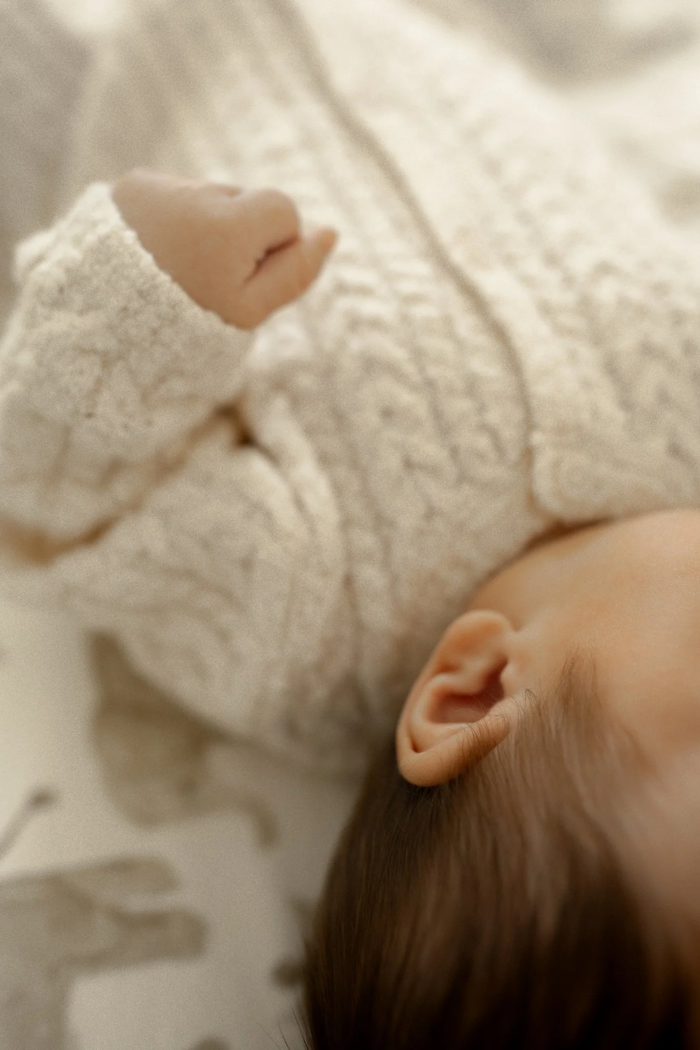Close-up of a sleeping baby's face and hand, lying on a soft blanket.