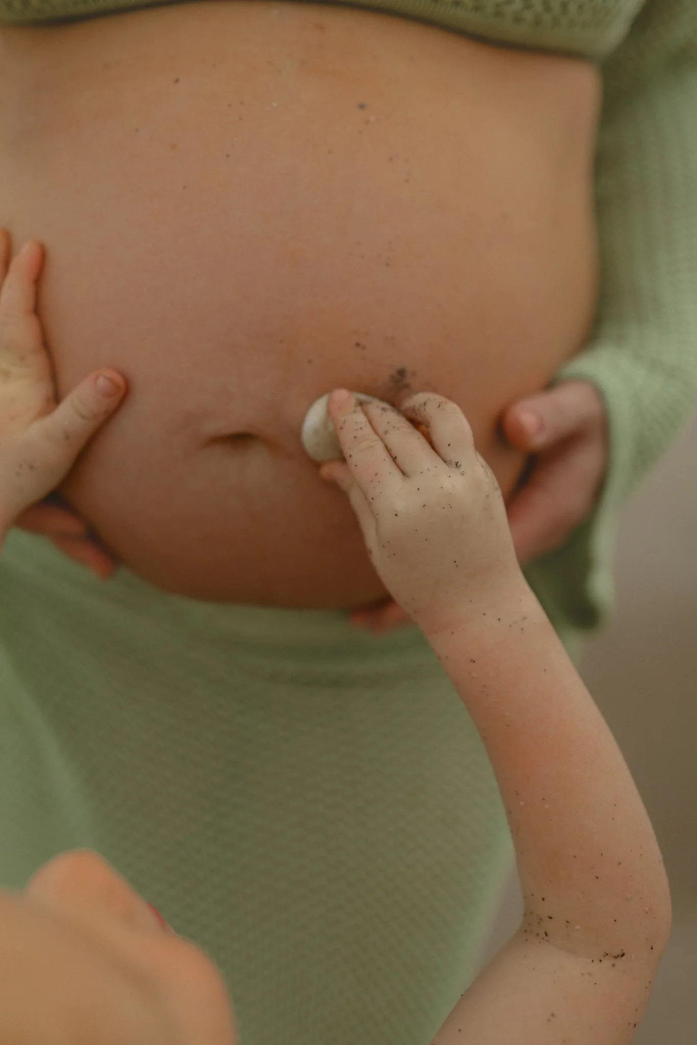 a pregnant belly with hands placing a shell next to the belly button