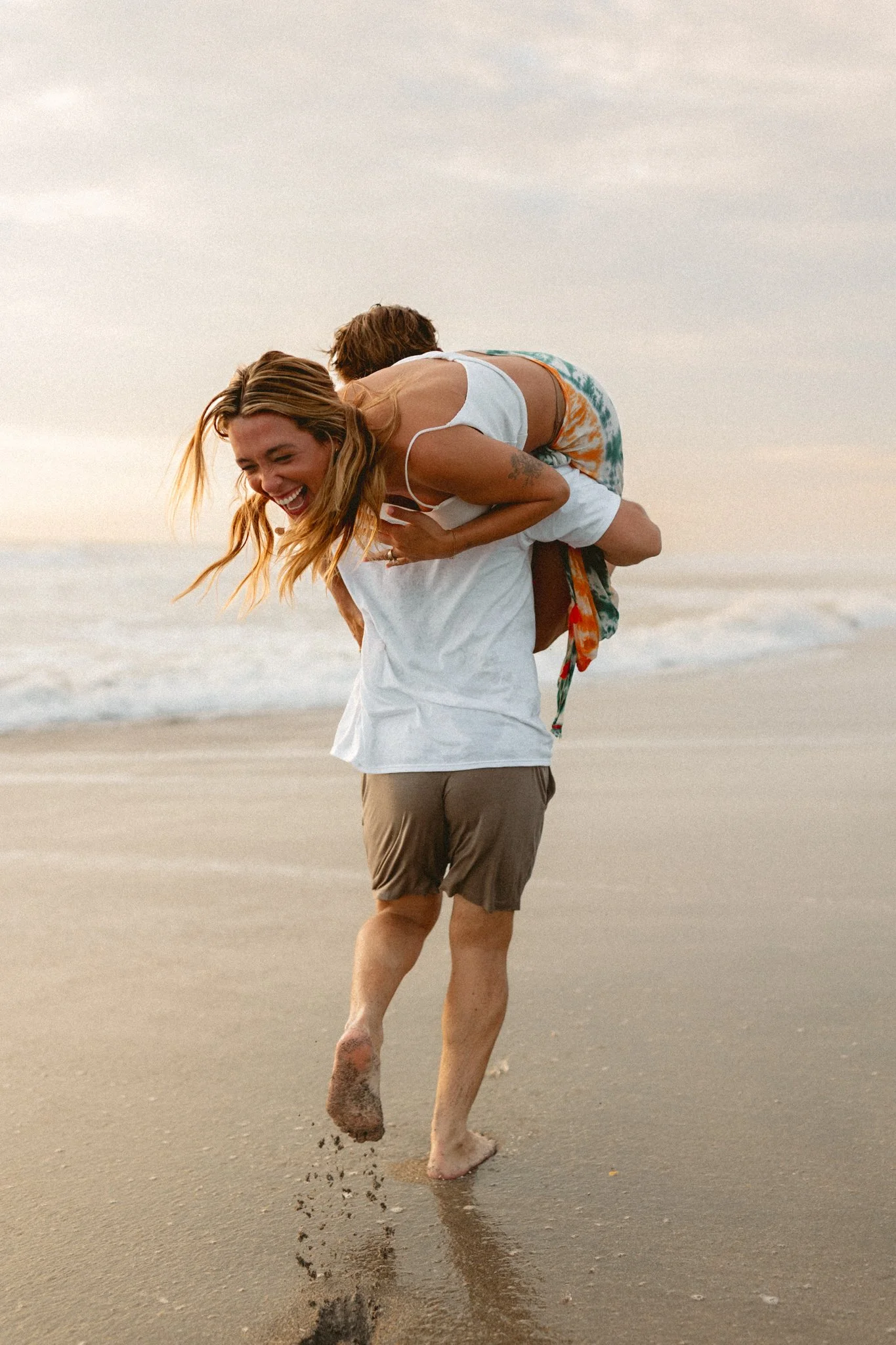 A man carrying a woman on the beach, both smiling and enjoying the moment
