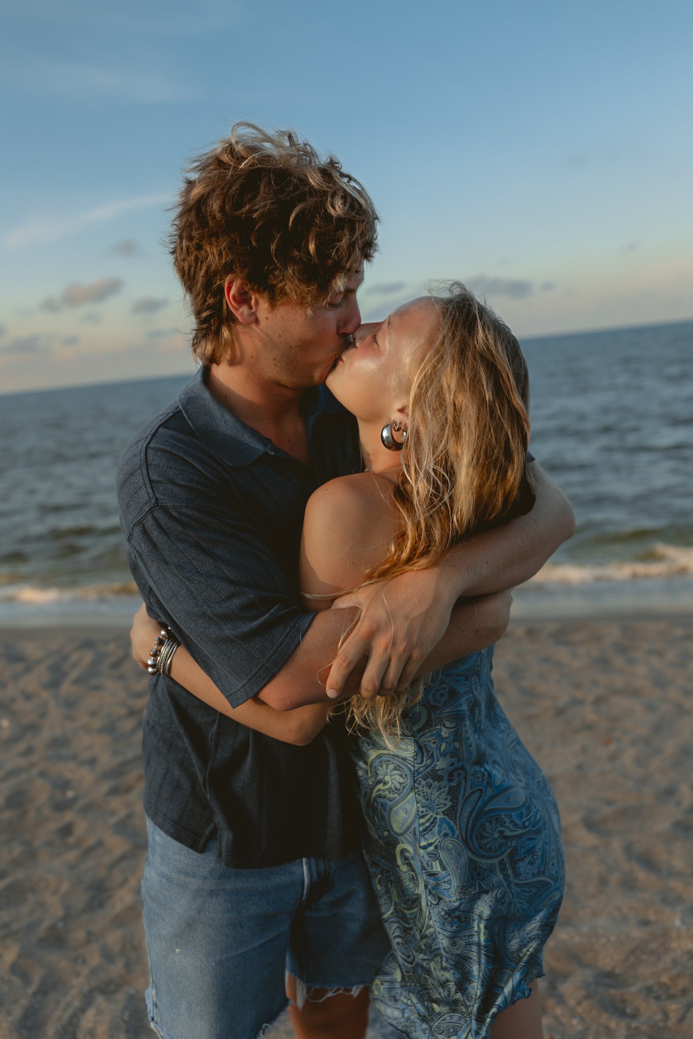 A young couple kissing and embracing on the beach during sunset.
