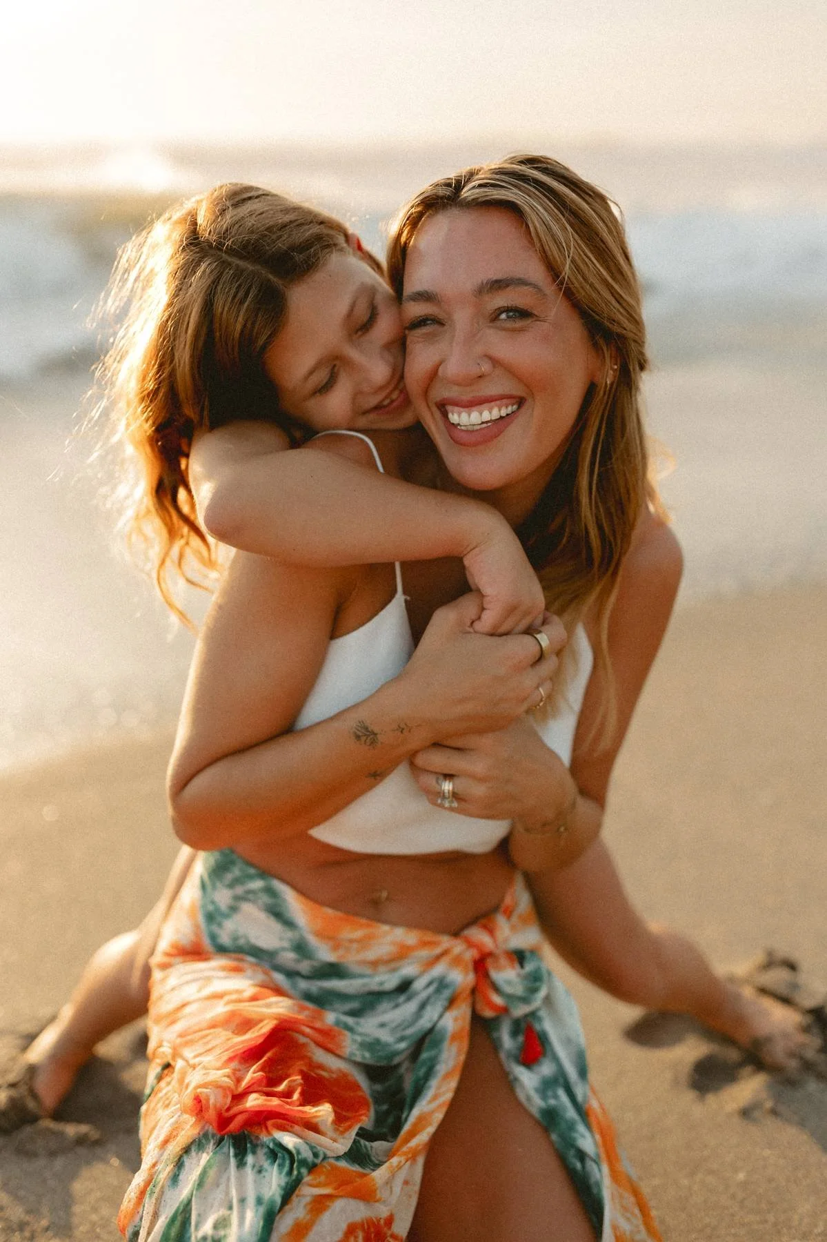 A woman and a girl sharing a hug on the beach during sunset.