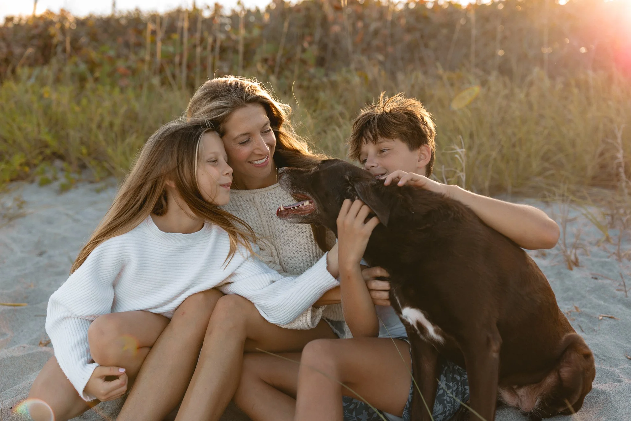 a mother with her young son and daughter petting their dog in front of the dunes during golden hour